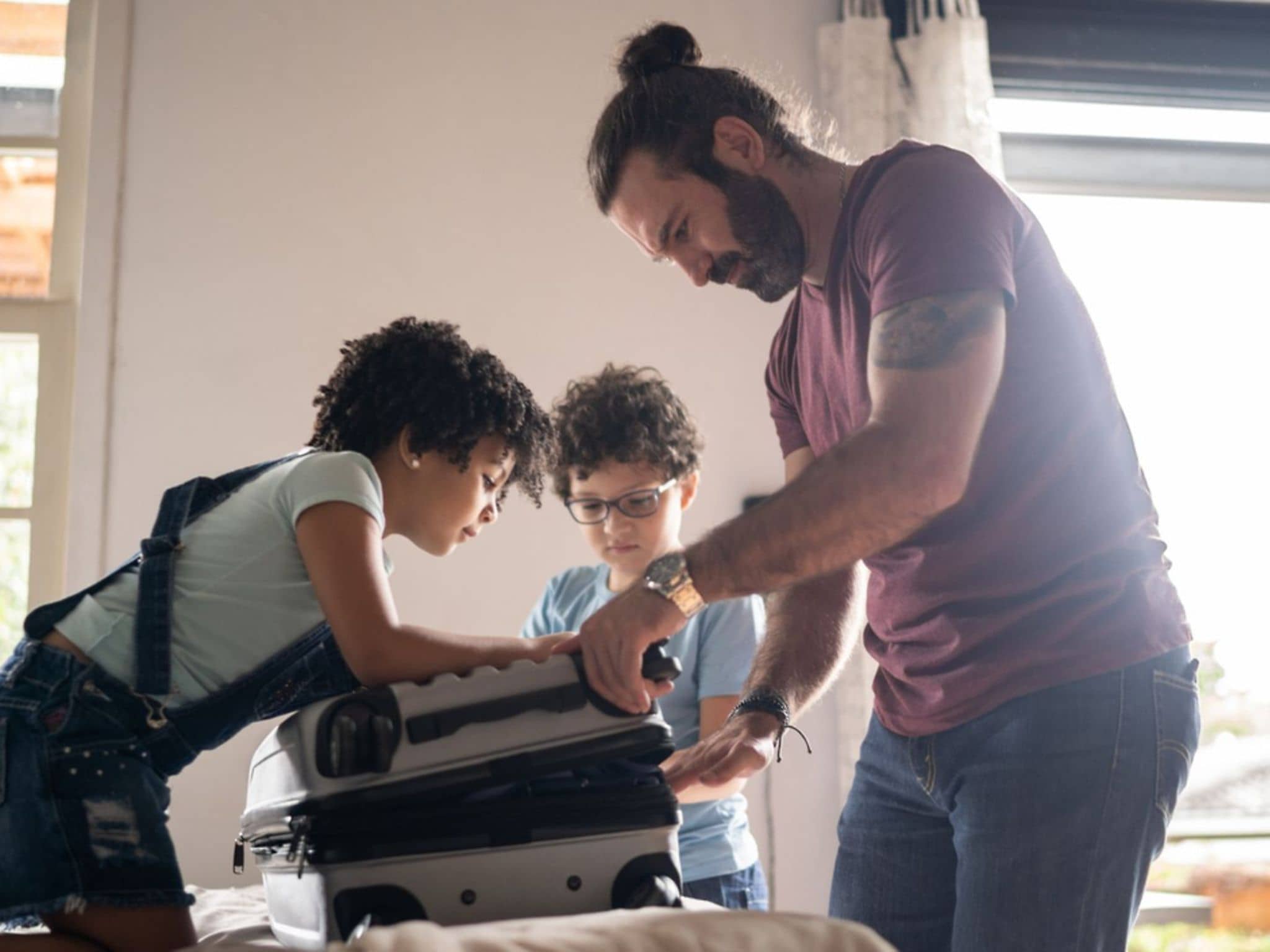 Vorbereitung Urlaub: Ein Vater packt mit zwei Kindern einen Koffer.