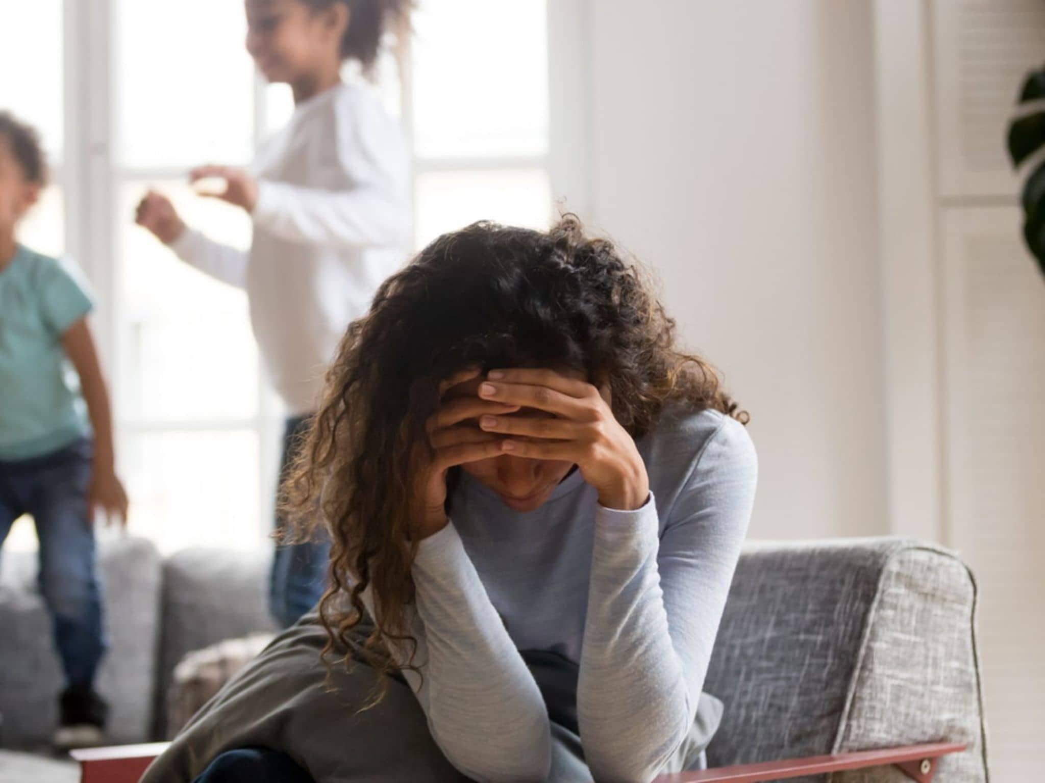 Eine Frau hält die Hände vors Gesicht, im Hintergrund spielen Kinder