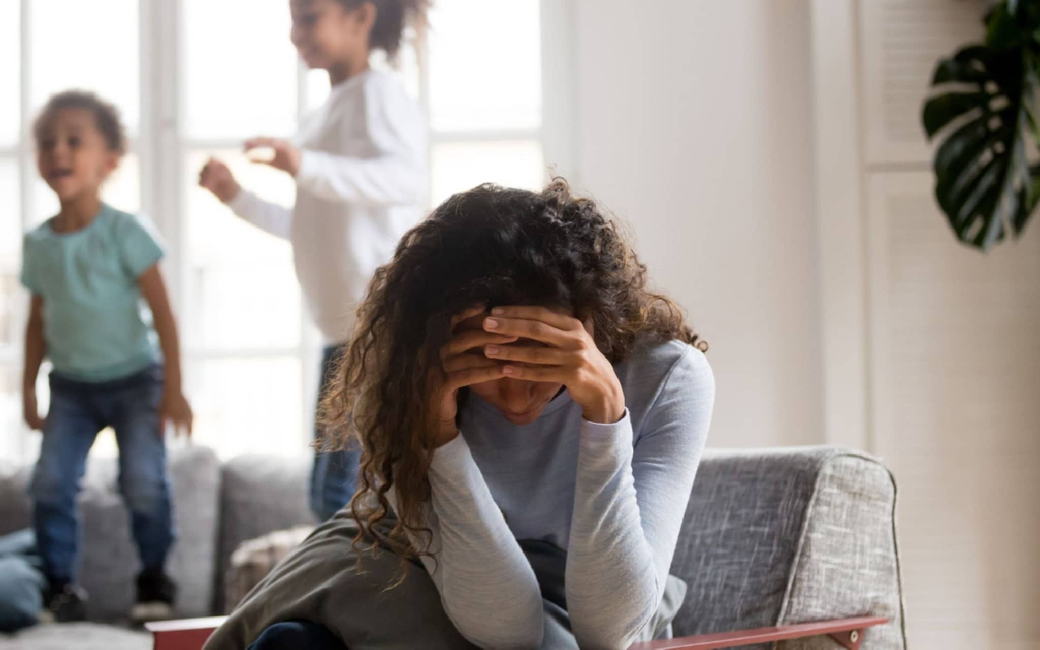 Eine Frau hält die Hände vors Gesicht, im Hintergrund spielen Kinder