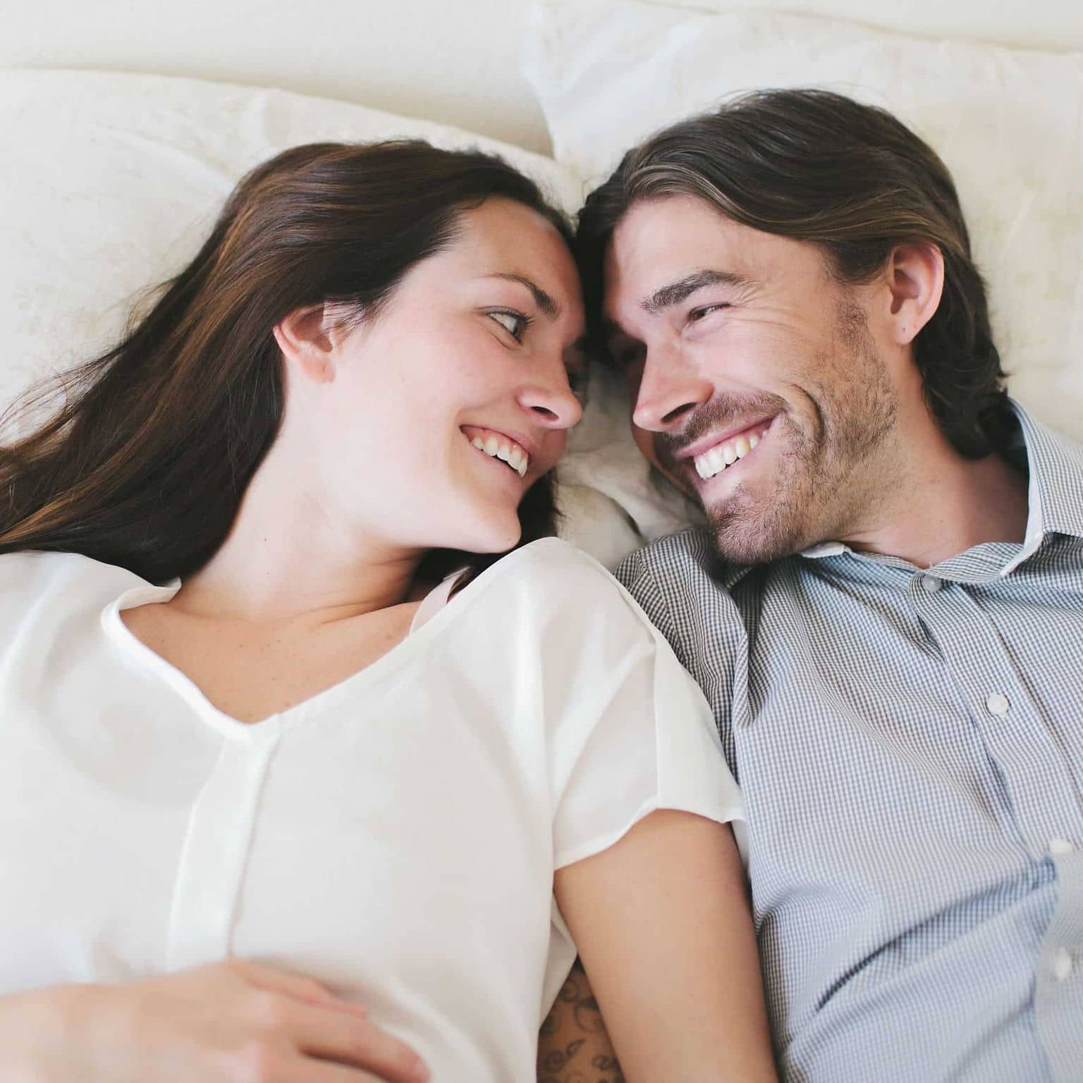 Vorsorgeuntersuchung Erwachsene: Mann und Frau lachen sich an im Bett.