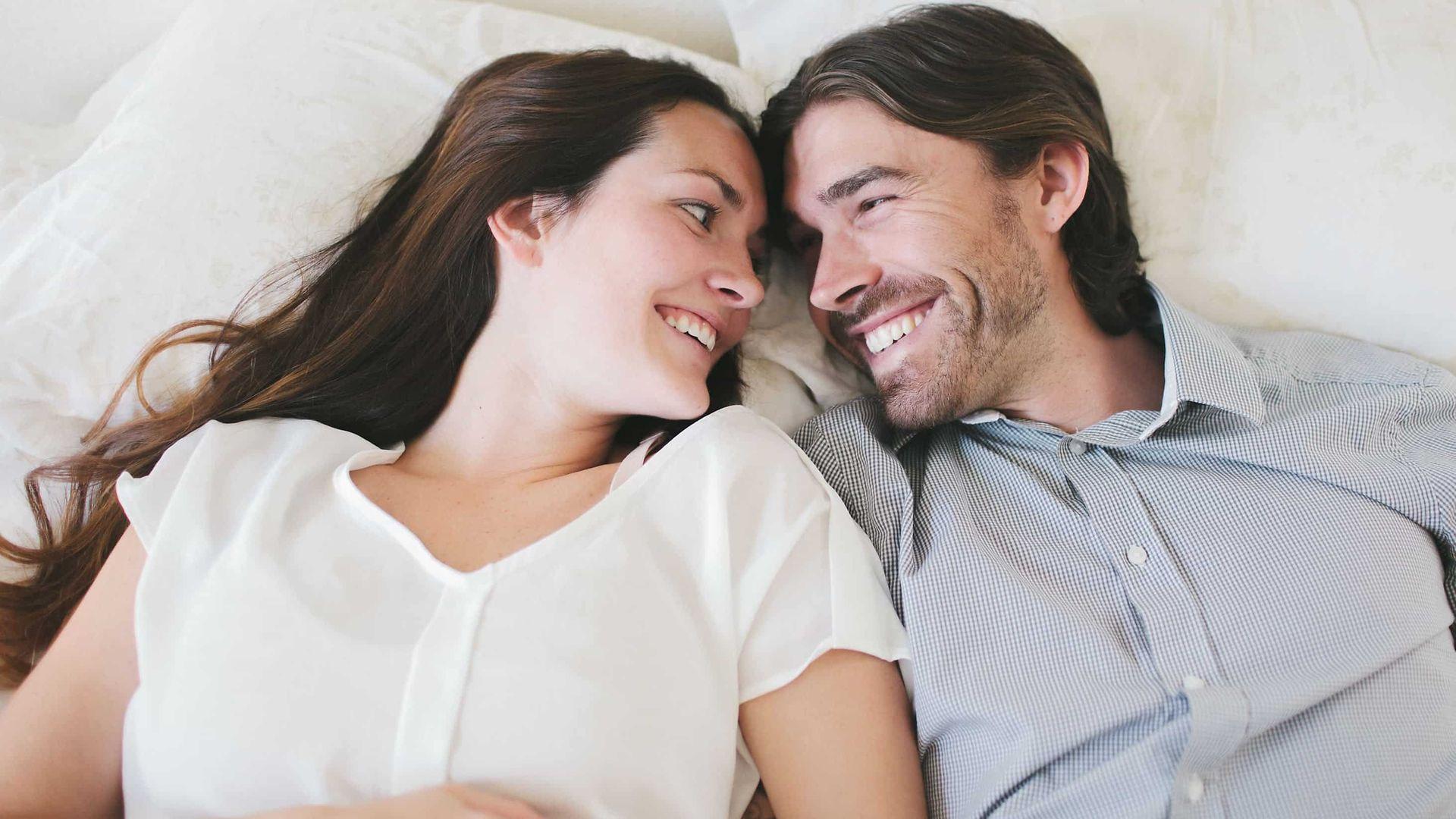 Vorsorgeuntersuchung Erwachsene: Mann und Frau lachen sich an im Bett.