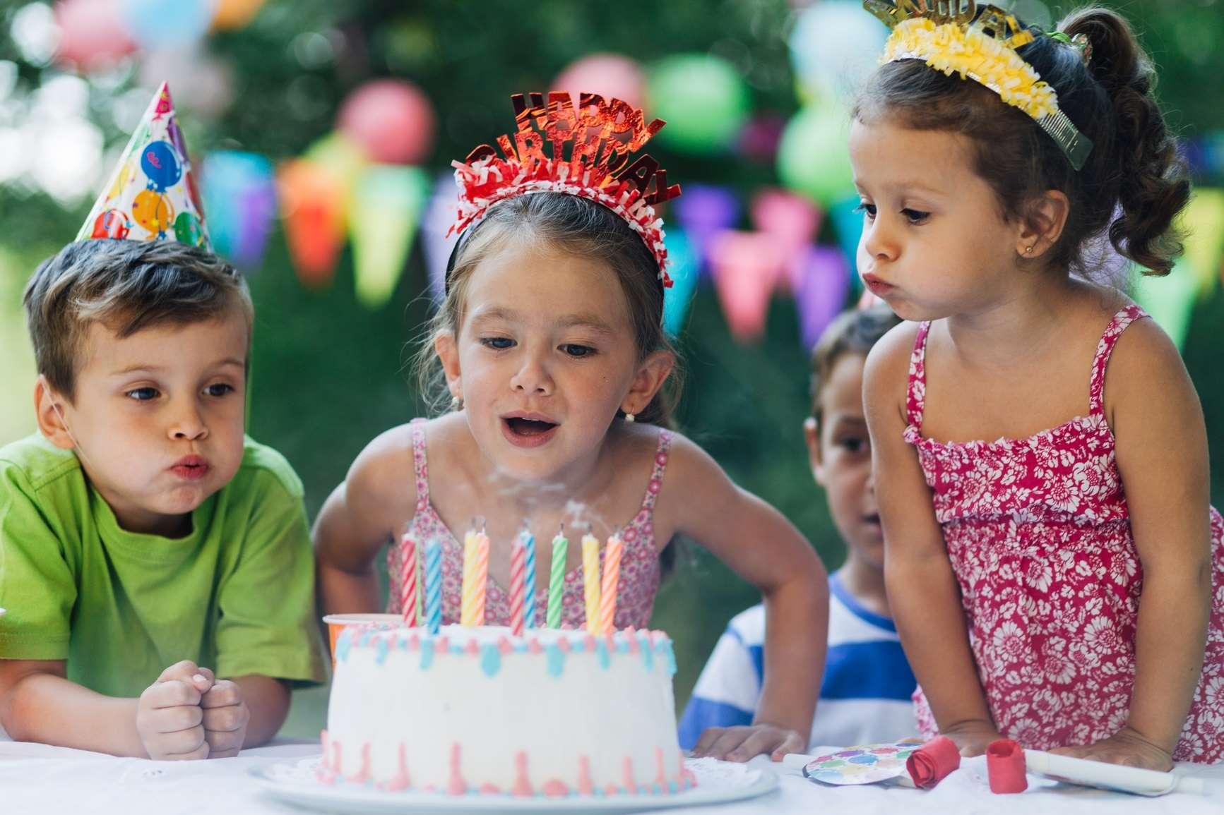 Vorsorgeuntersuchung Kinder: Mädchen bläst Geburtstagskerzen aus.hen lächelt zufrieden auf grüner Wiese.