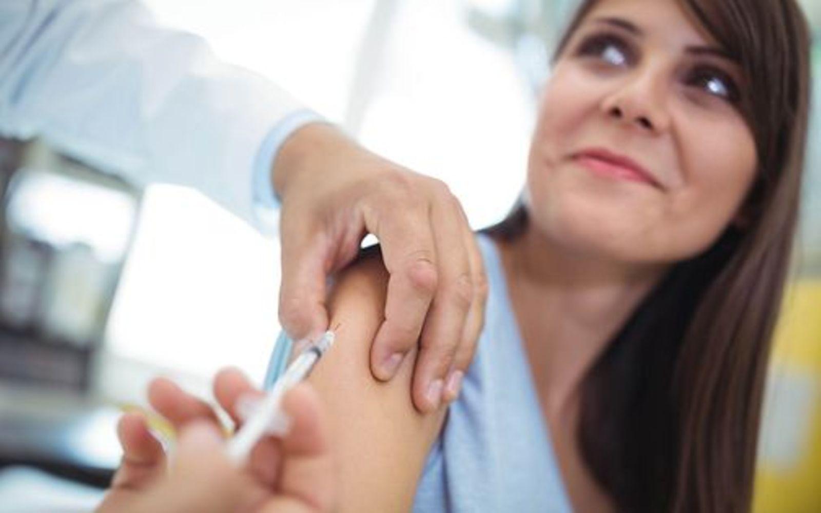 Impfungen für Erwachsene: Junge Frau erhält Spritze in den Oberarm.