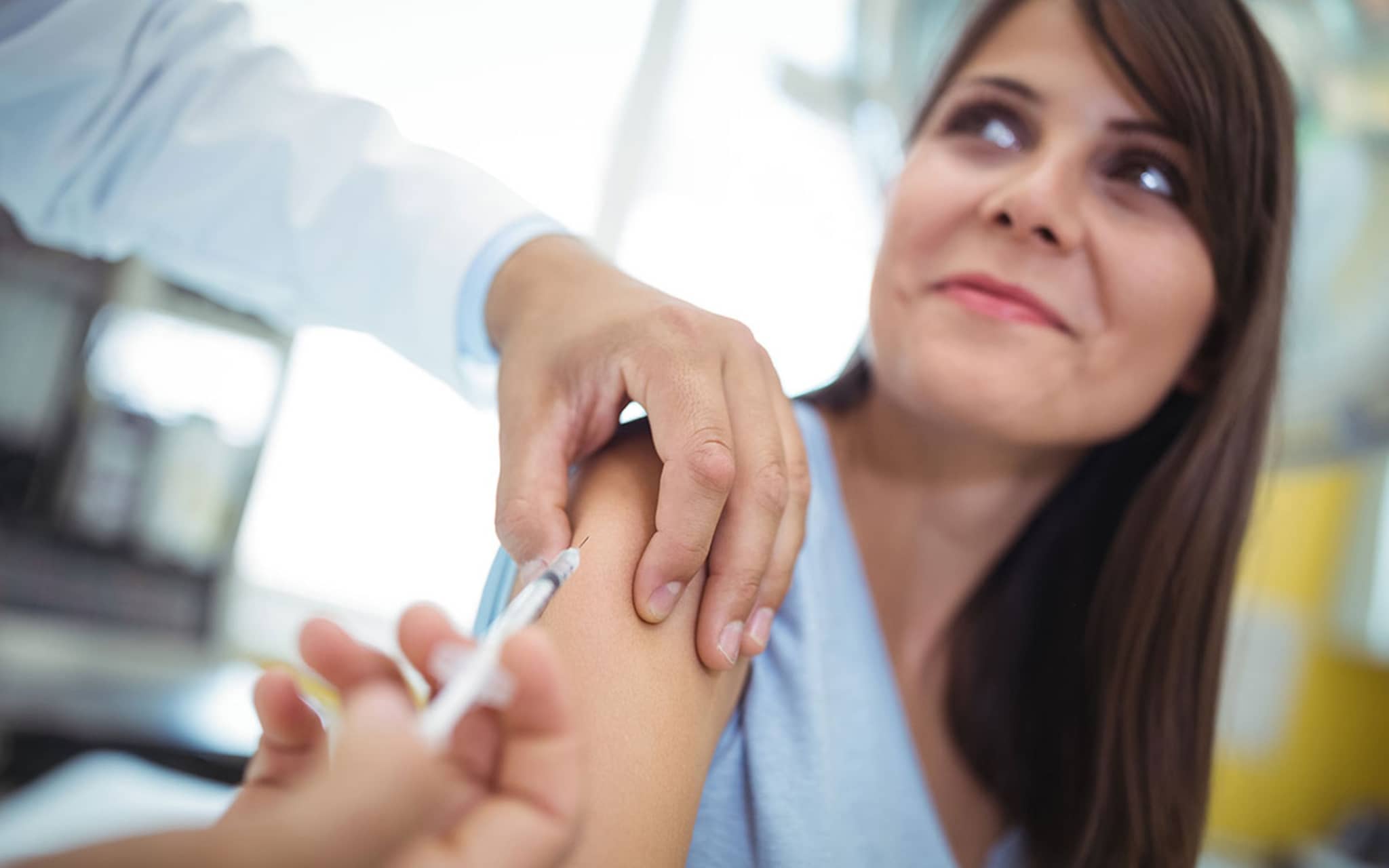 Impfungen für Erwachsene: Junge Frau erhält Spritze in den Oberarm.