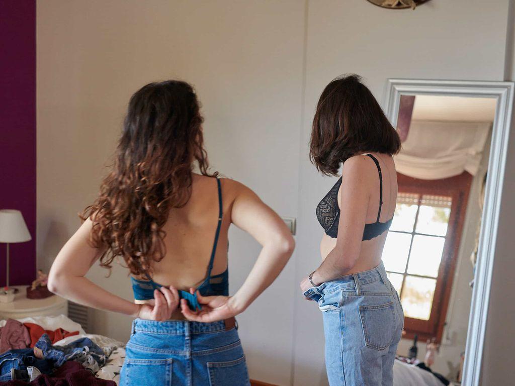 Magersucht:  Zwei Frauen in Jeans und BH betrachten sich im Spiegel.