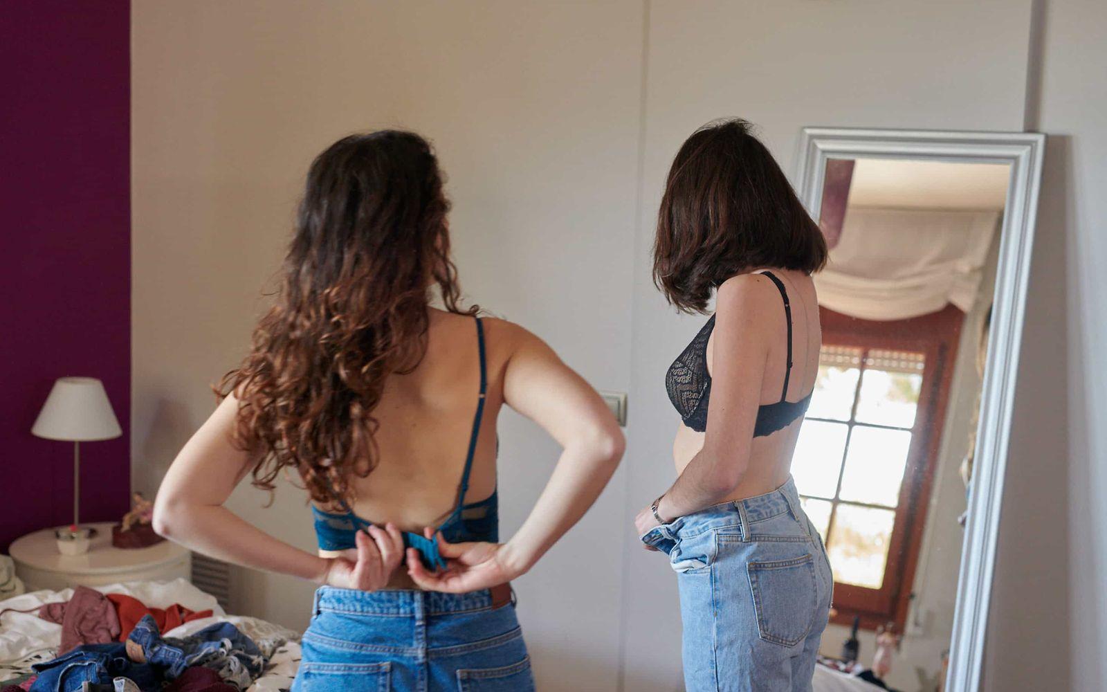 Magersucht:  Zwei Frauen in Jeans und BH betrachten sich im Spiegel.