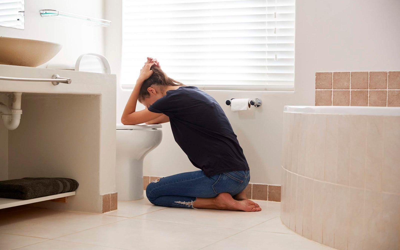 Bulimie: Frau kniet gebeugt vor der Toilette.