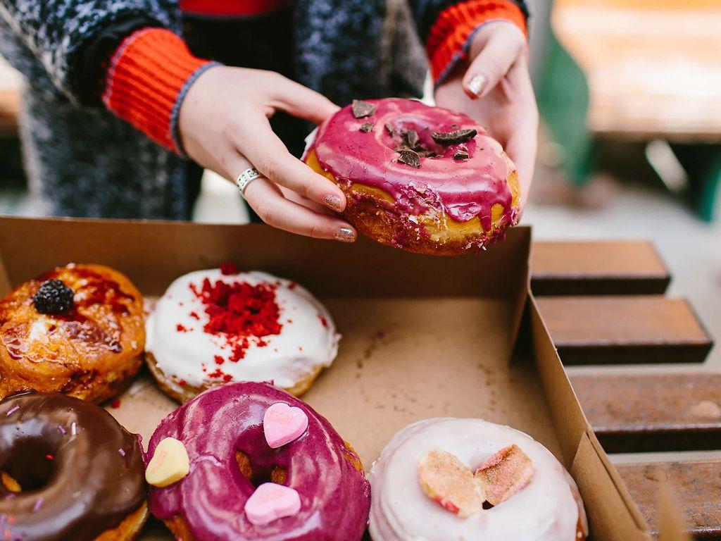 Binge Eating: Karton mit bunt glasierten Donuts.