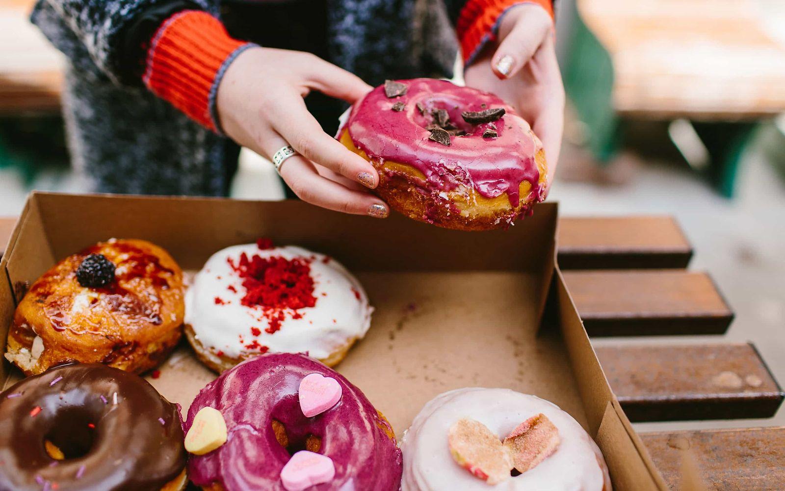 Binge Eating: Karton mit bunt glasierten Donuts.