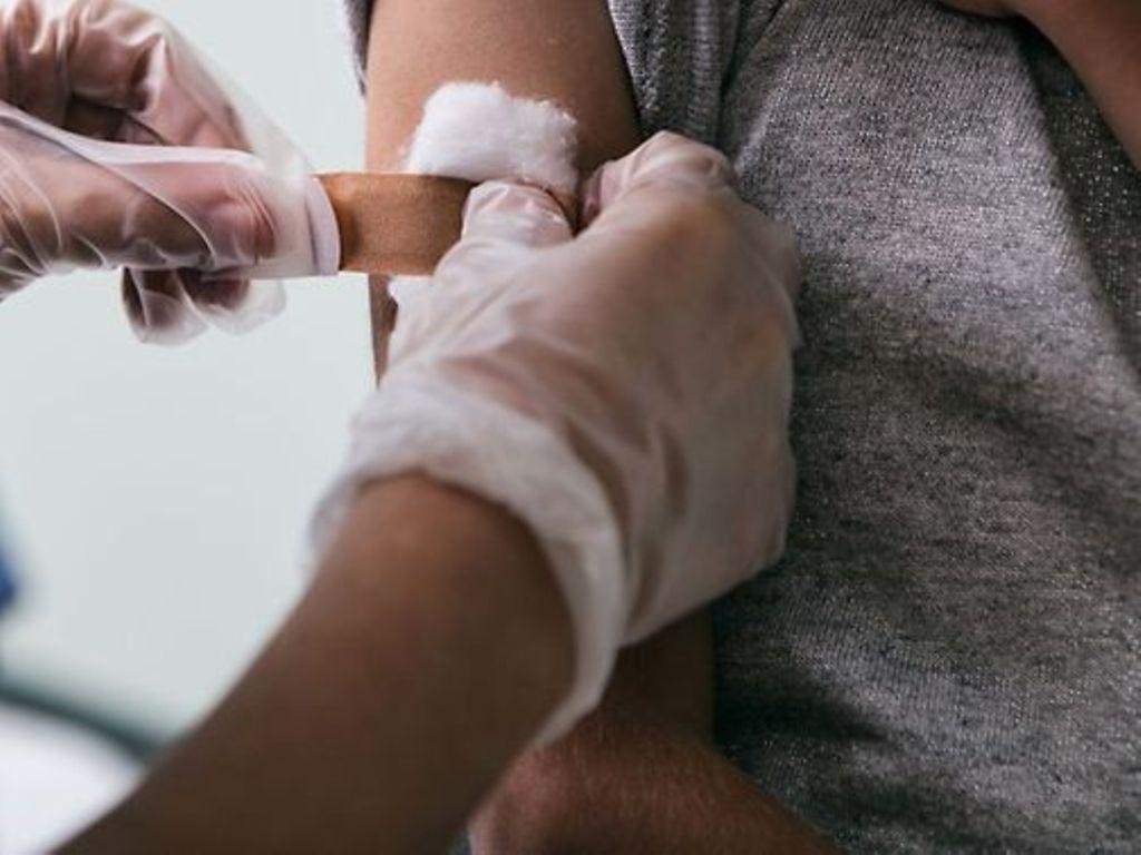 HPV-Impfung: Hände in Einmalhandschuhen kleben Pflaster auf einen Arm. 