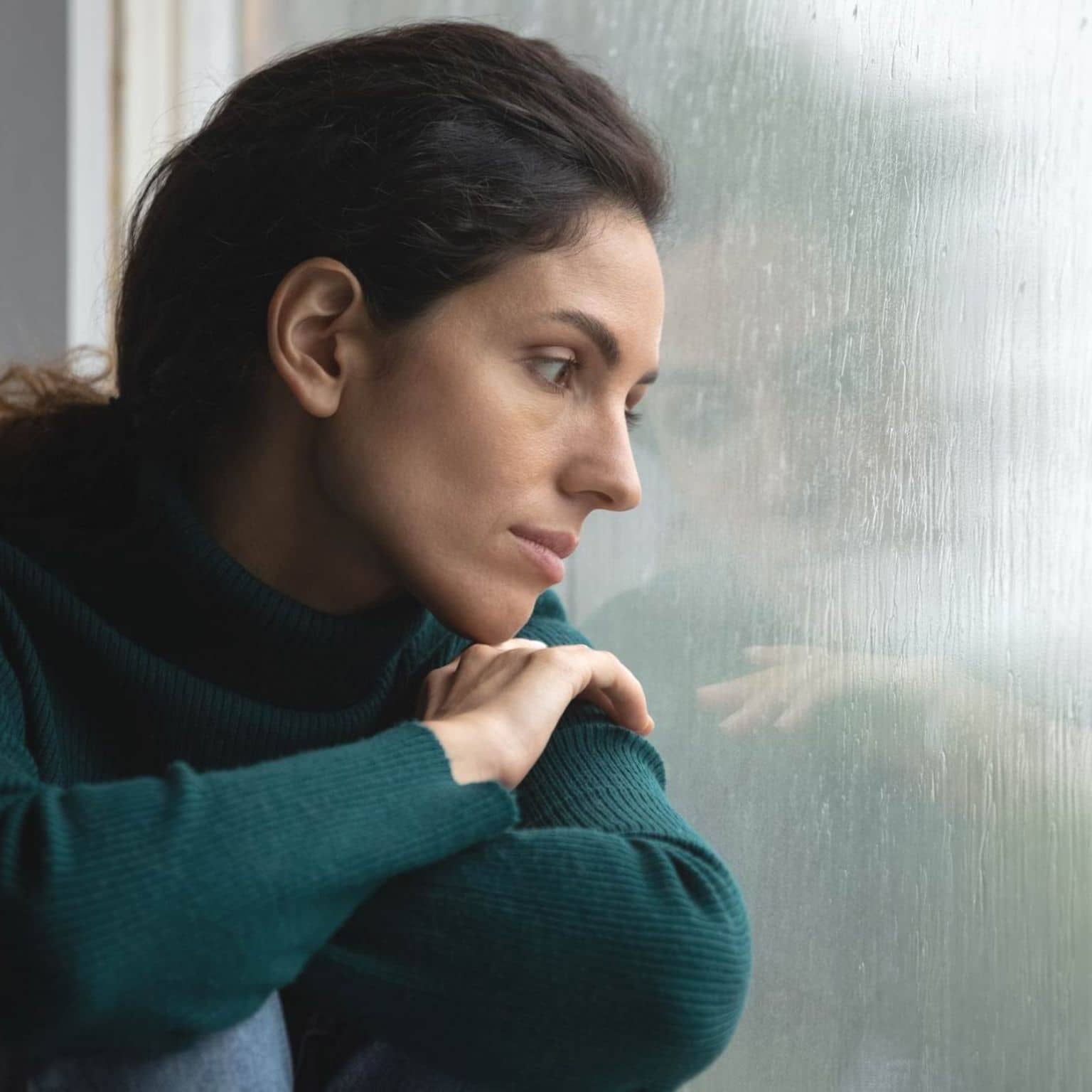 Psychotherapie: Frau sitzt am Fenster und schaut in den Regen.