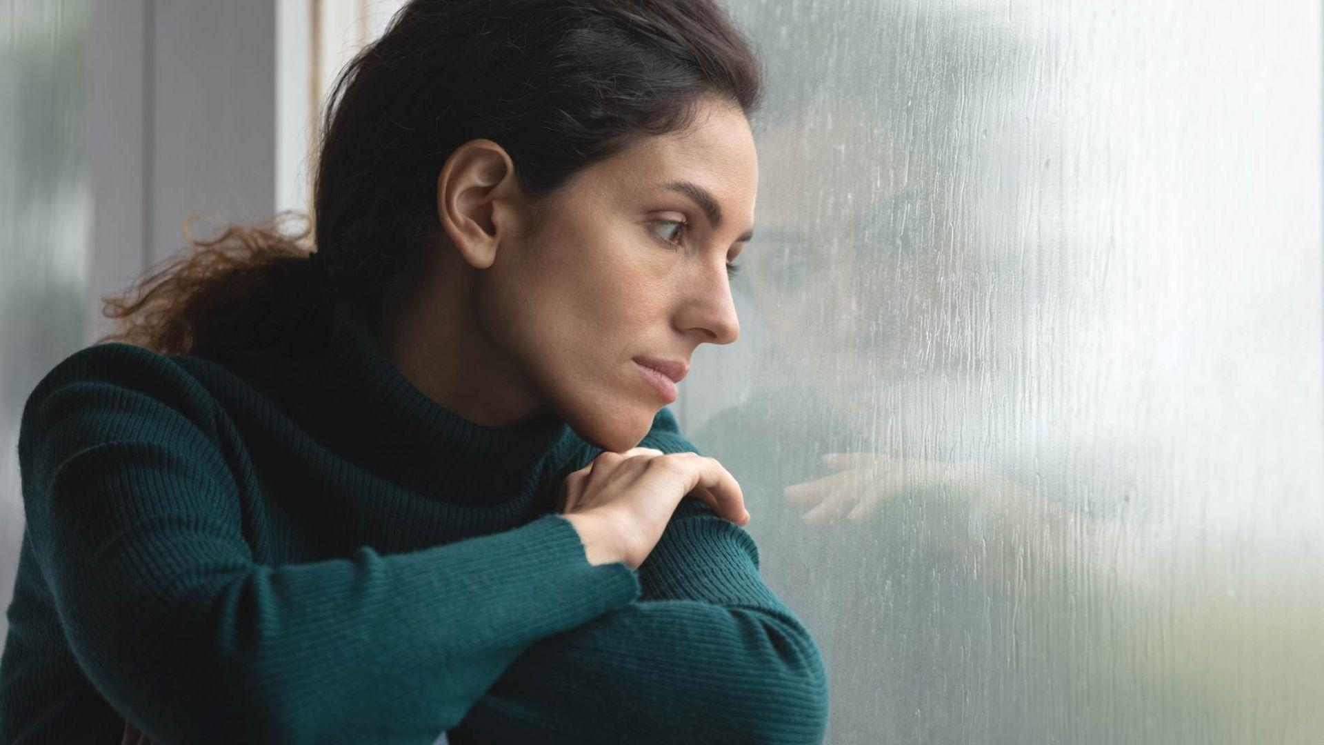 Psychotherapie: Frau sitzt am Fenster und schaut in den Regen.