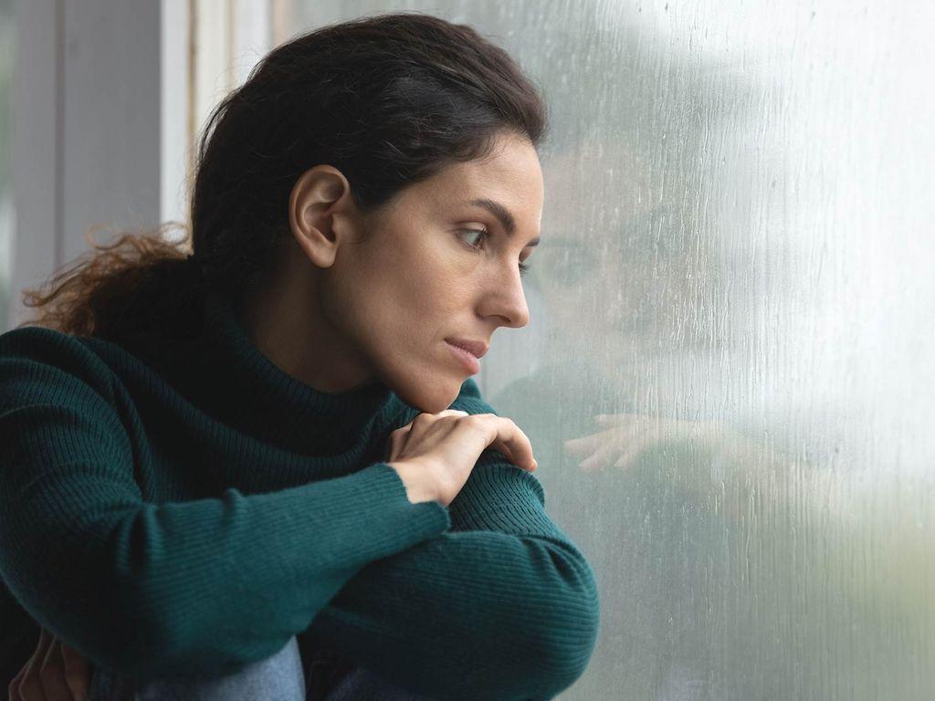 Psychotherapie: Frau sitzt am Fenster und schaut in den Regen.