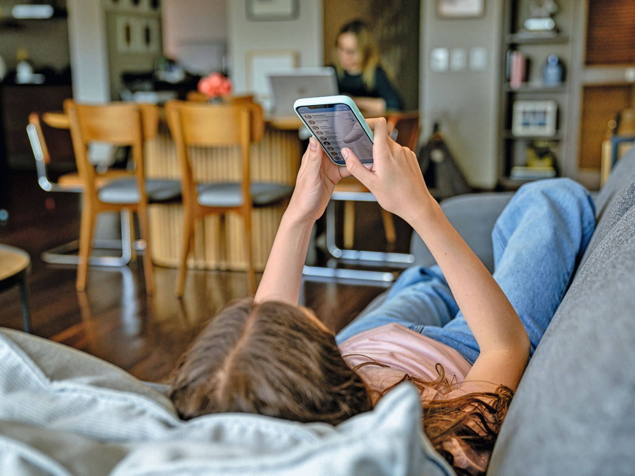 Bild: Person auf Sofa mit Handy in den Händen. Wohn Essbereich