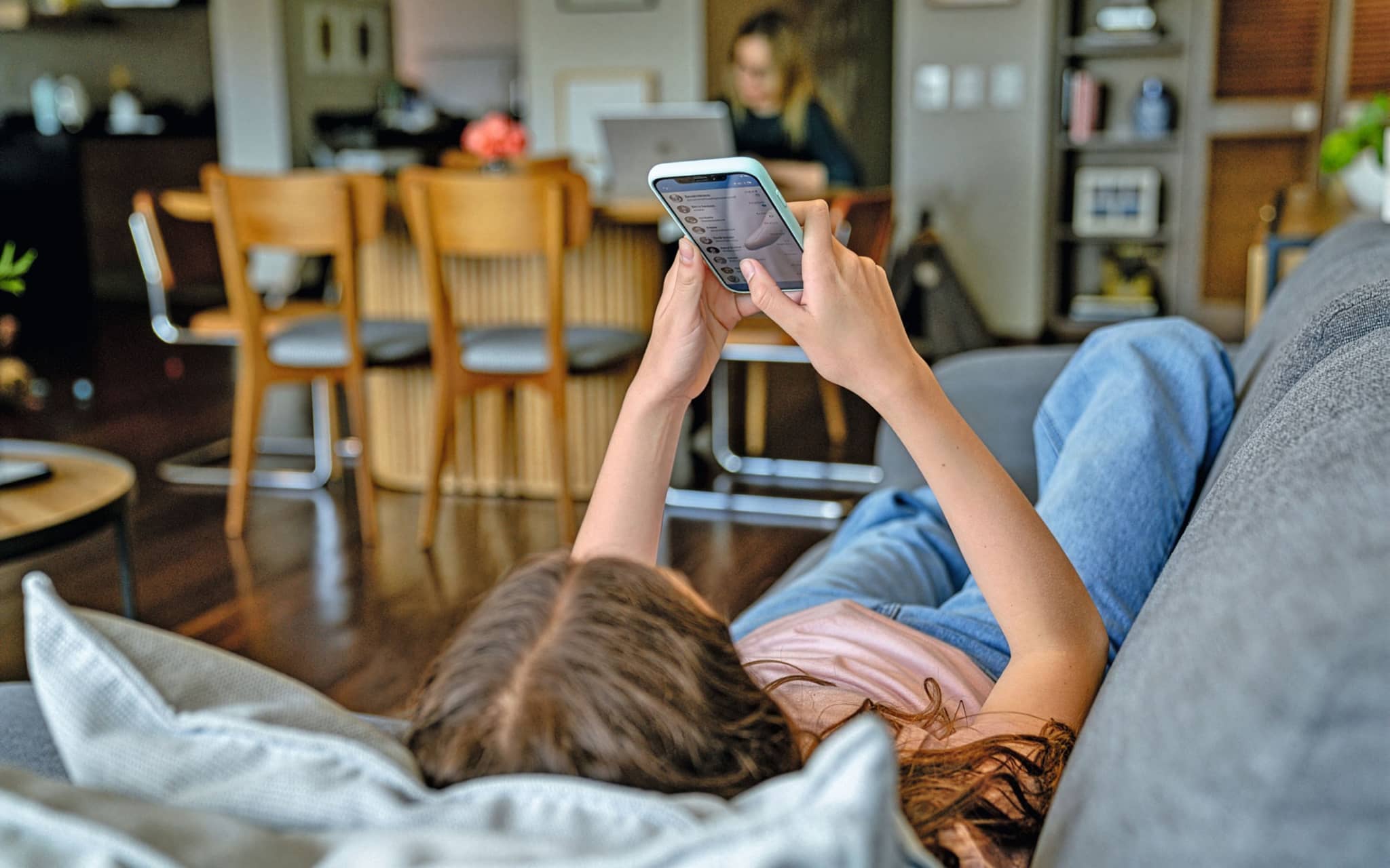 Bild: Person auf Sofa mit Handy in den Händen. Wohn Essbereich