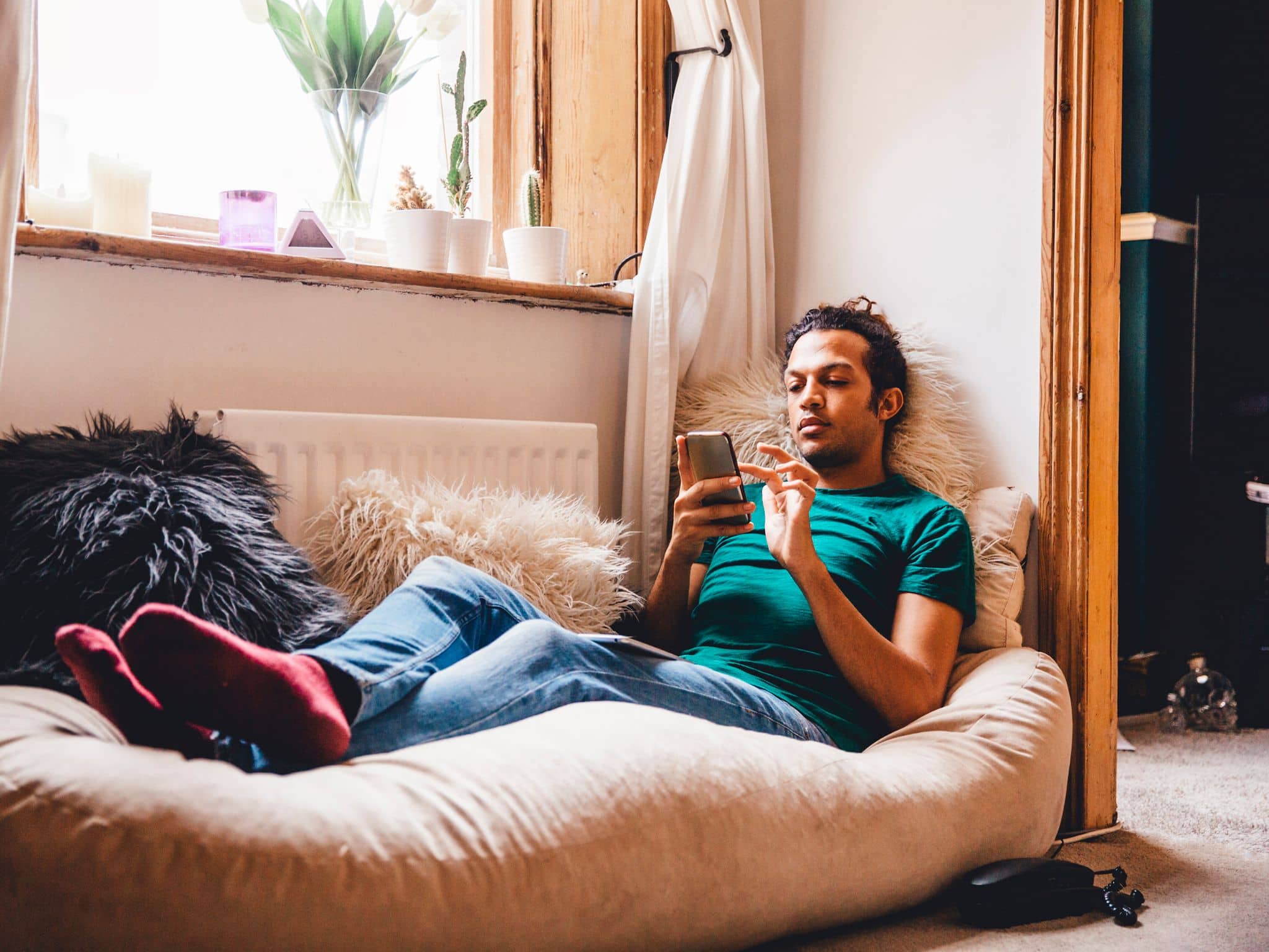 Junger Mann liegt entspannt auf Sitzsack und schaut auf sein Handy.