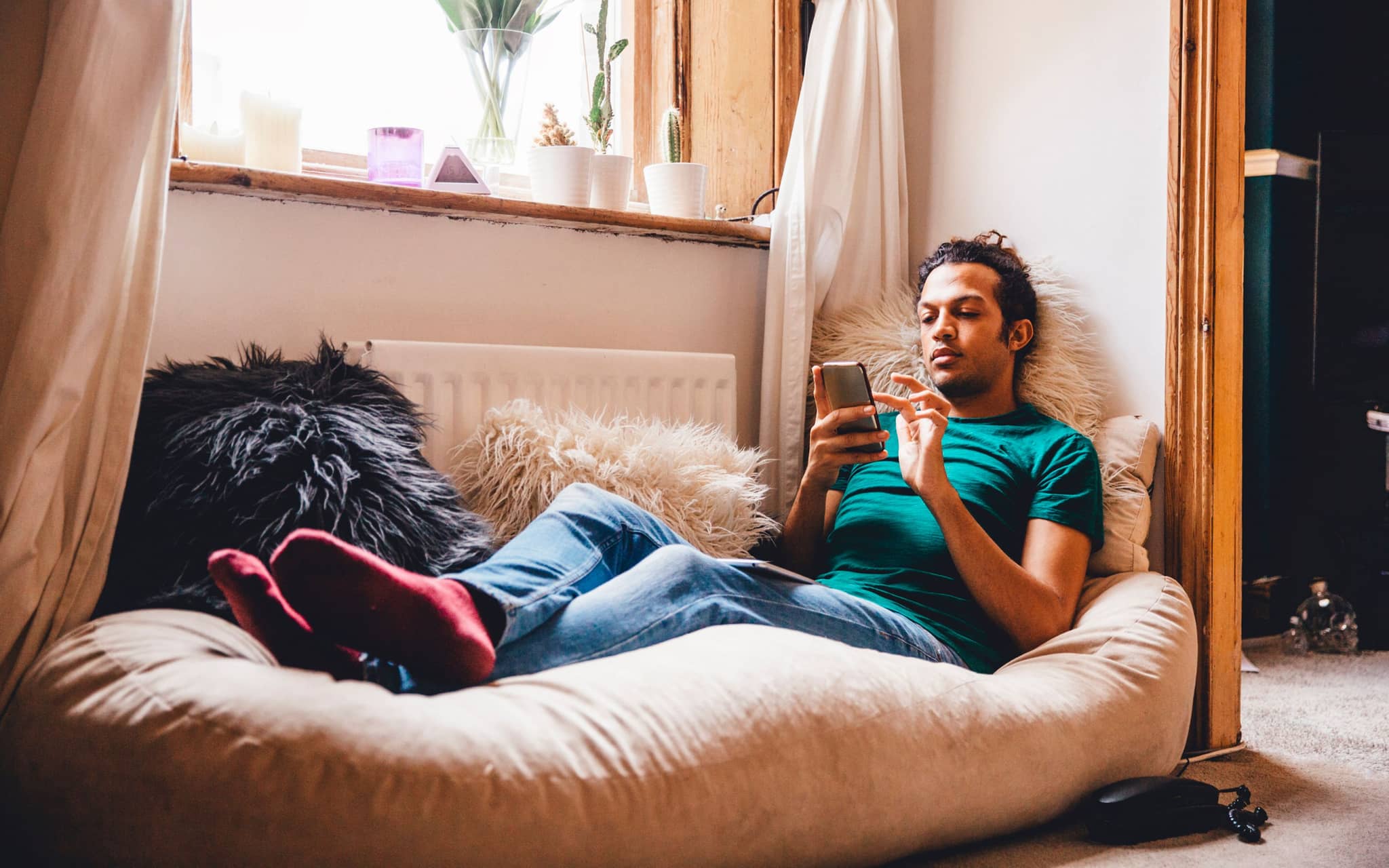 Junger Mann liegt entspannt auf Sitzsack und schaut auf sein Handy.
