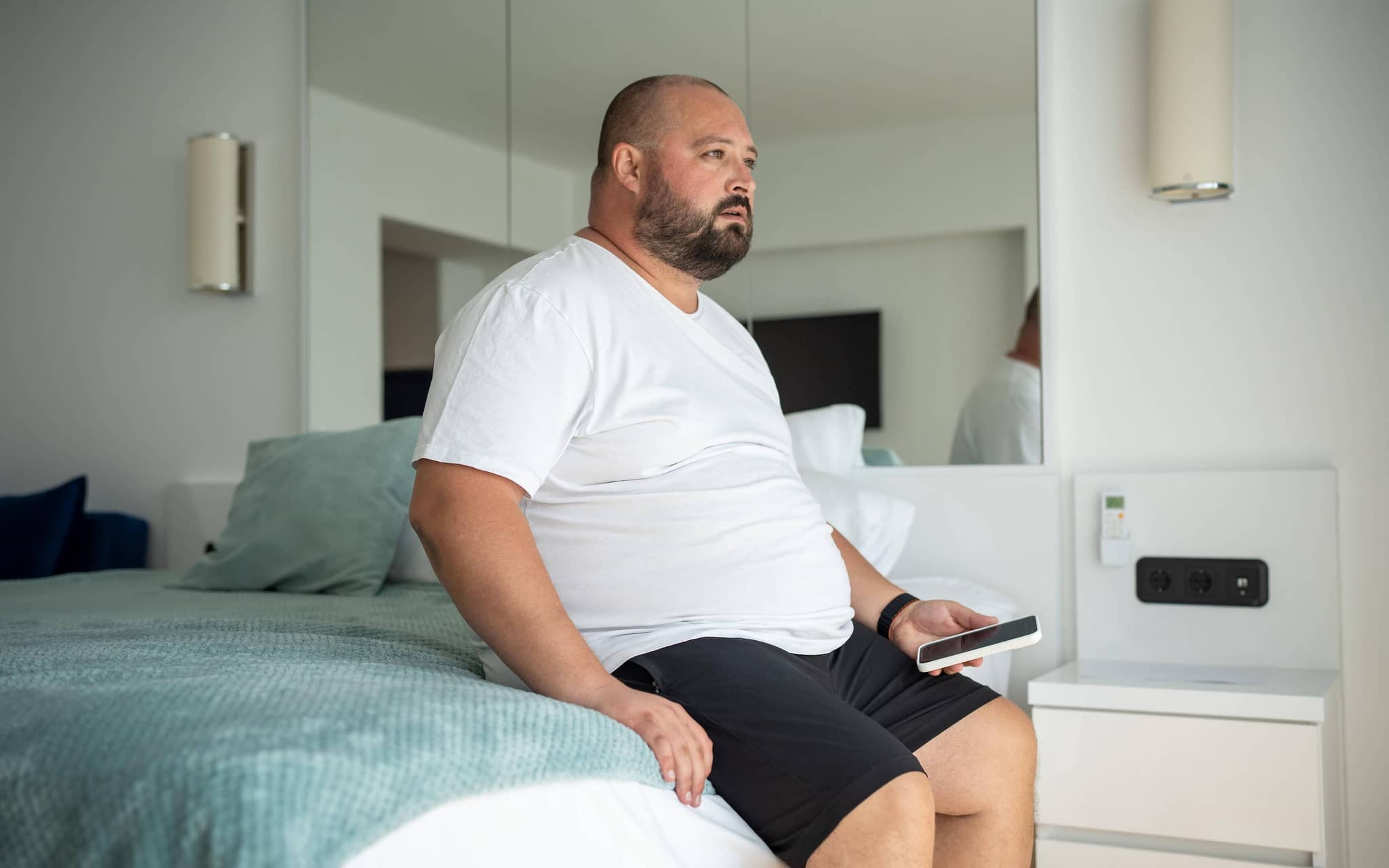 Korpulenter Mann sitzt auf seinem Bett.