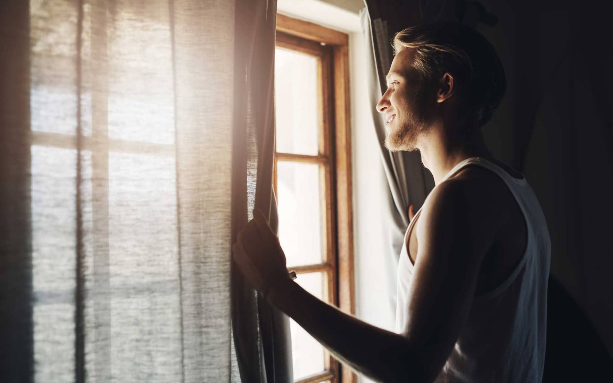 Junger Mann öffent am Morgen die Vorhänge am Fenster