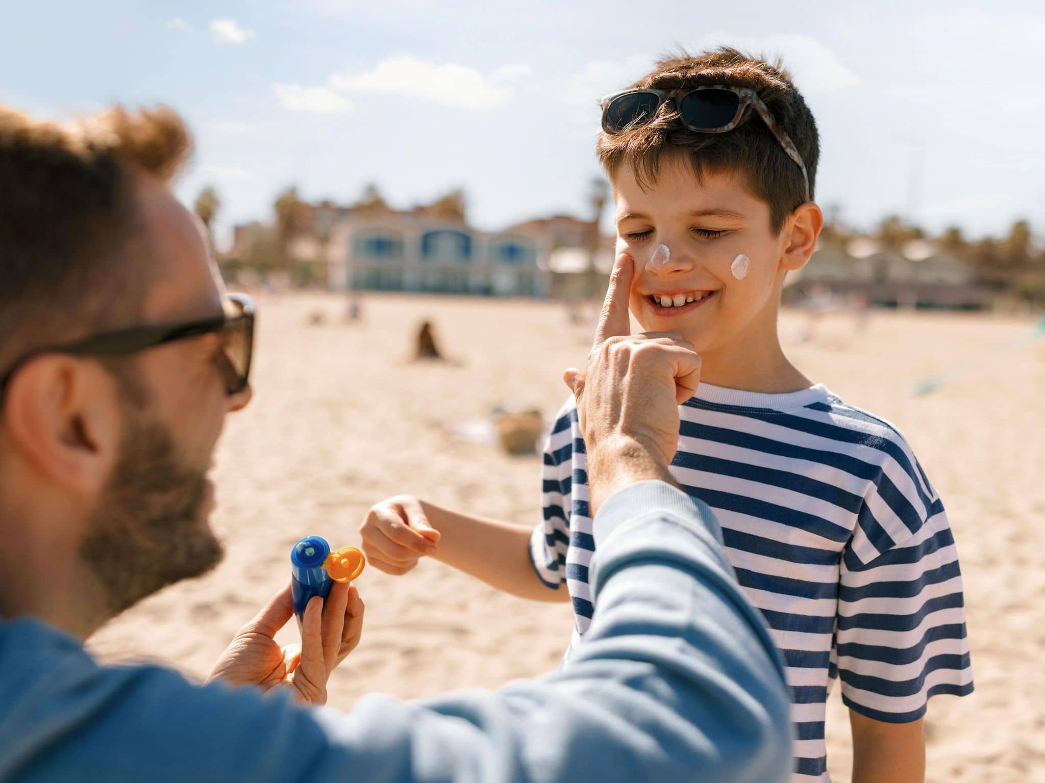 Ein Vater cremt seinen Sohn am Strand mit Sonnencreme ein.