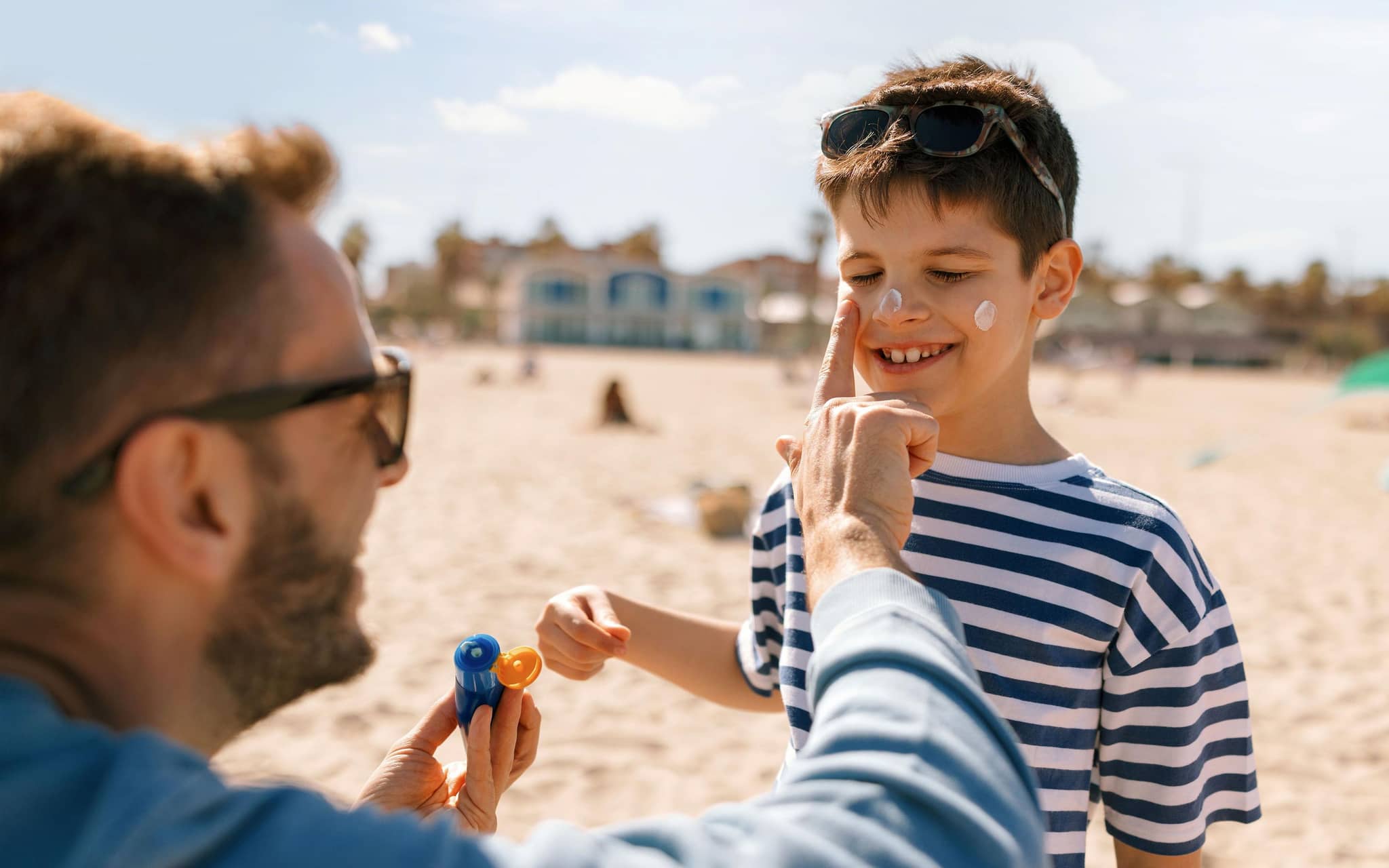 Ein Vater cremt seinen Sohn am Strand mit Sonnencreme ein.