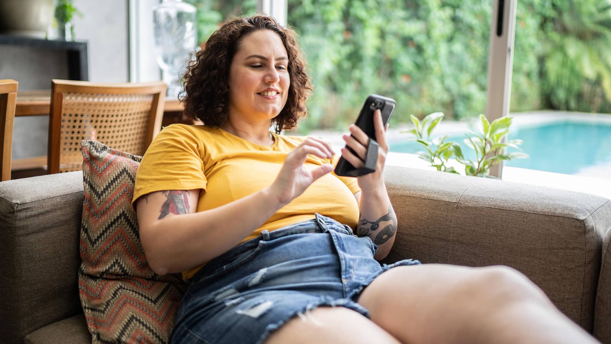 Korpulente Frau bedient ihr Smartphone auf der Couch.
