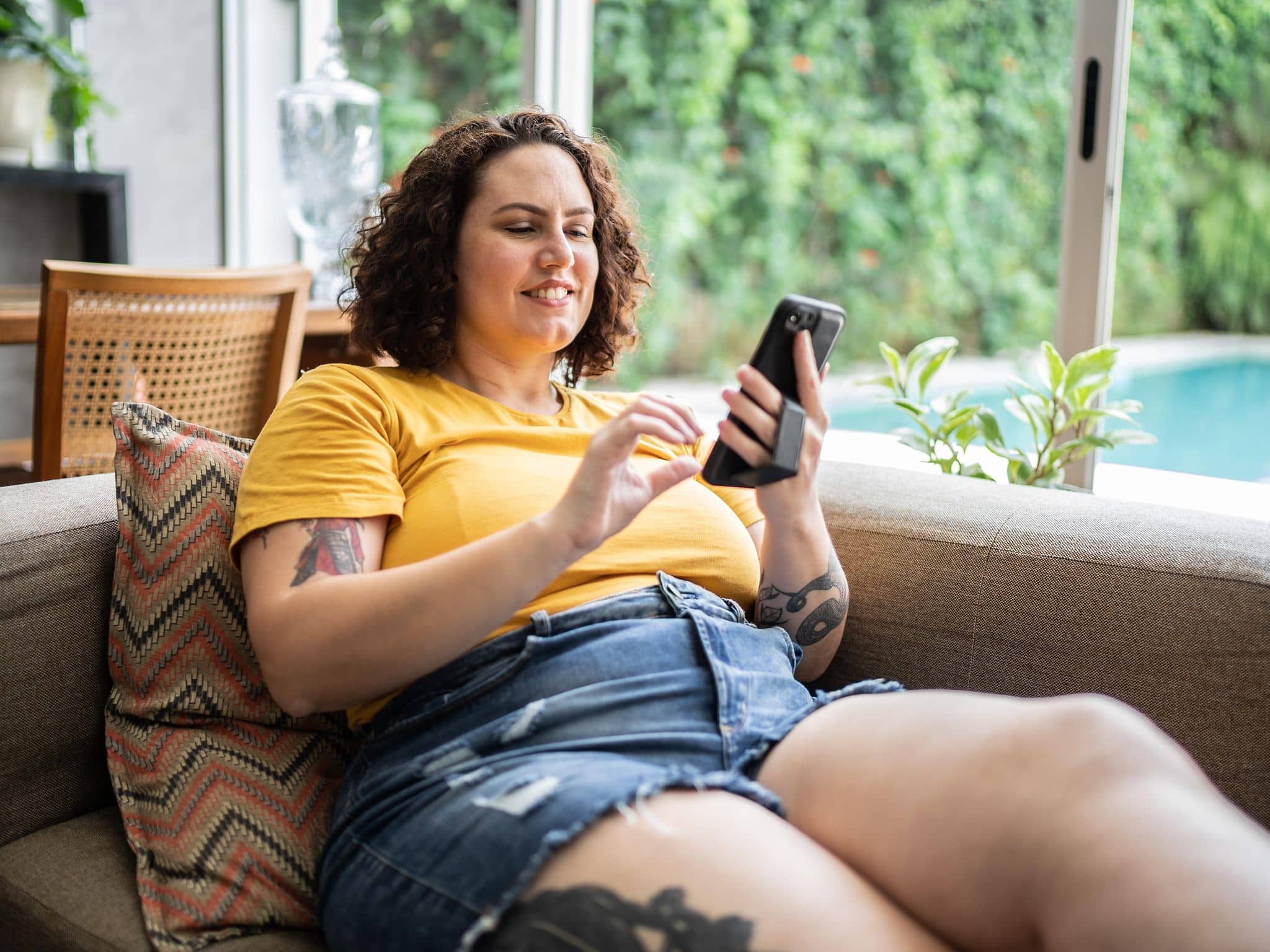 Korpulente Frau bedient ihr Smartphone auf der Couch.