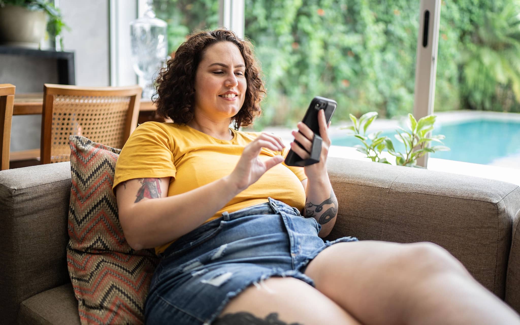 Korpulente Frau bedient ihr Smartphone auf der Couch.