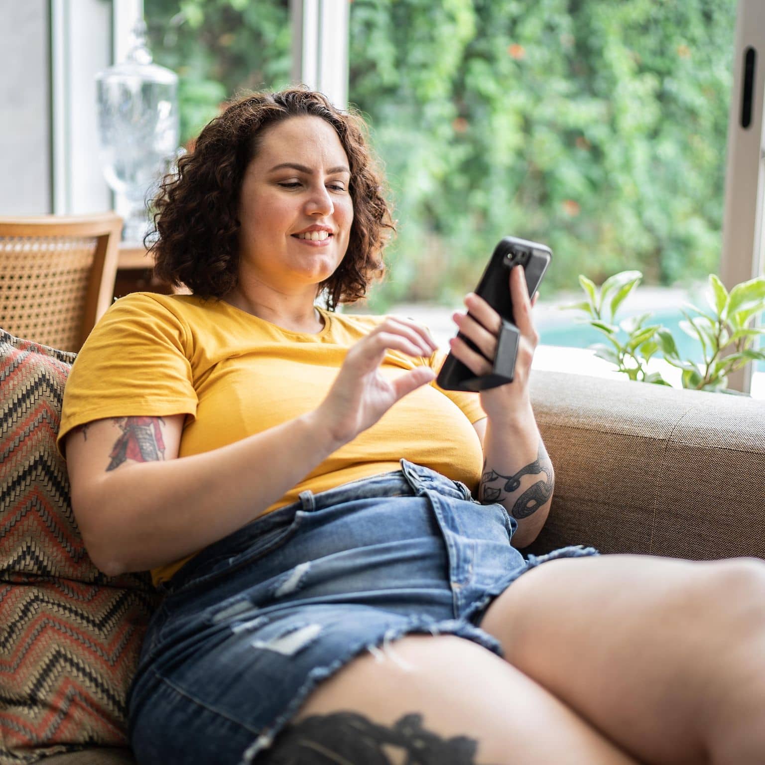 Korpulente Frau bedient ihr Smartphone auf der Couch.