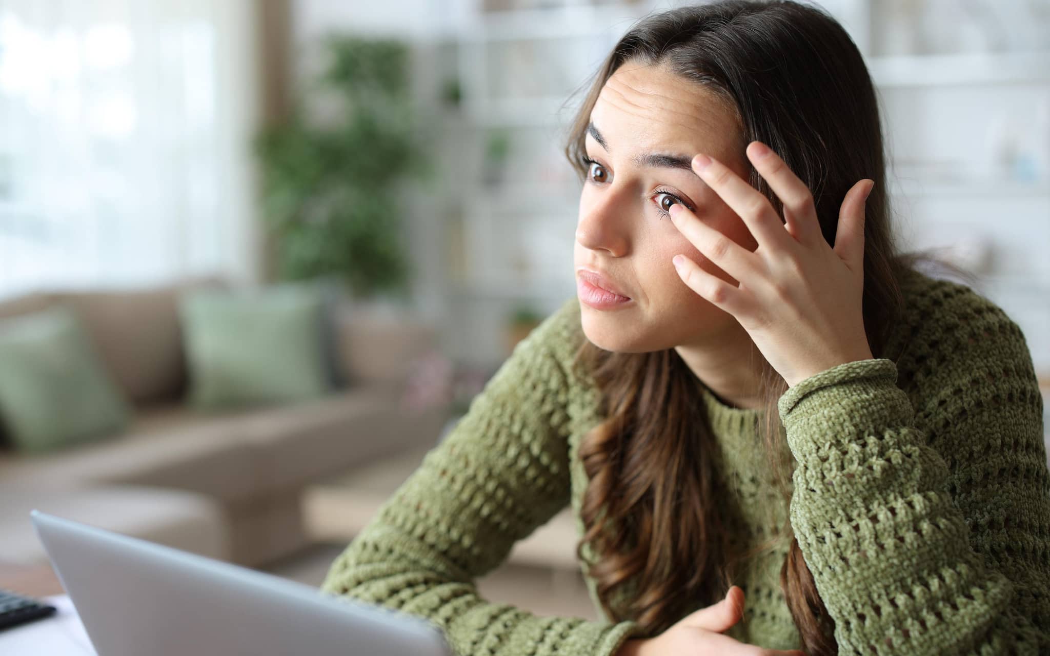 Frau fasst sich ins Auge während sie vorm Laptop sitzt.