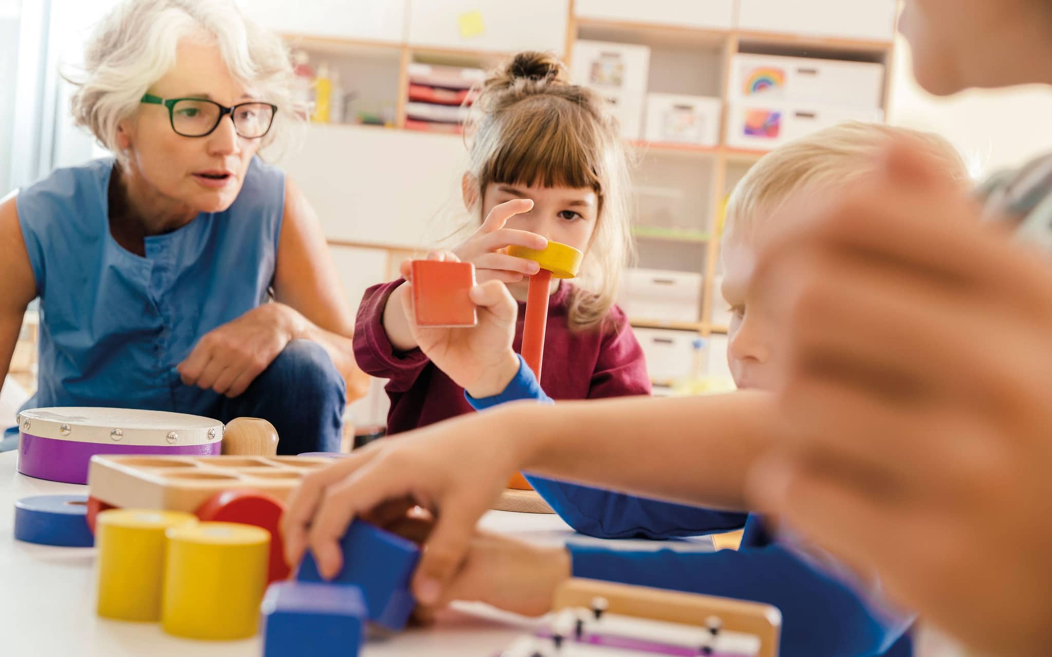 Ältere Frau arbeitet im Kindergarten mit Kindern.