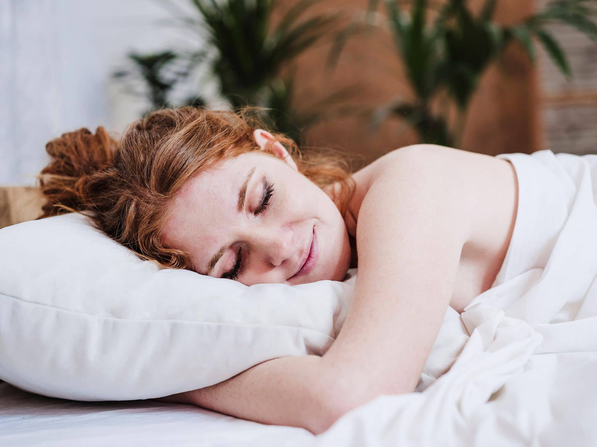 Nackte Frau schläft lächelnd im Bett.