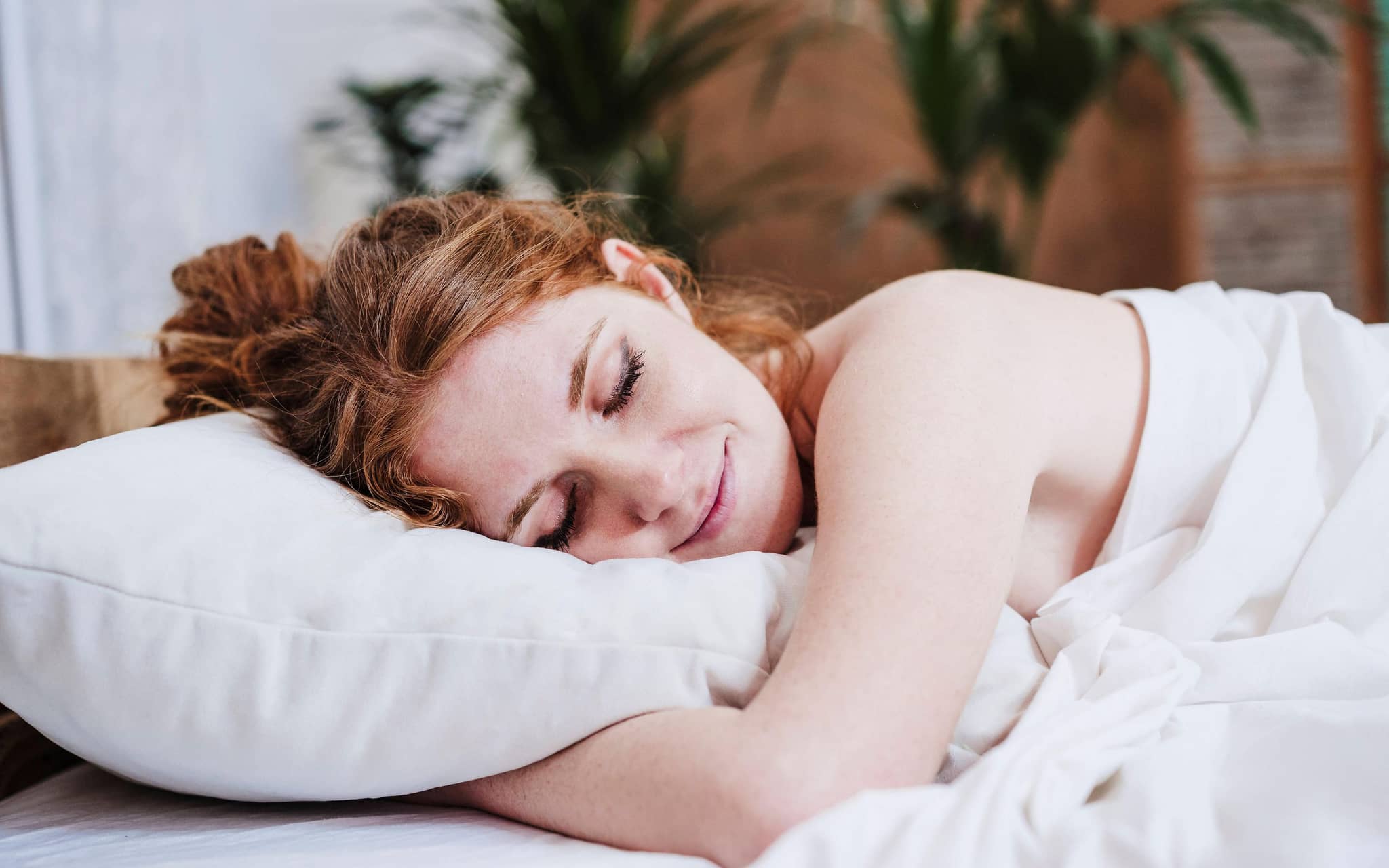 Nackte Frau schläft lächelnd im Bett.