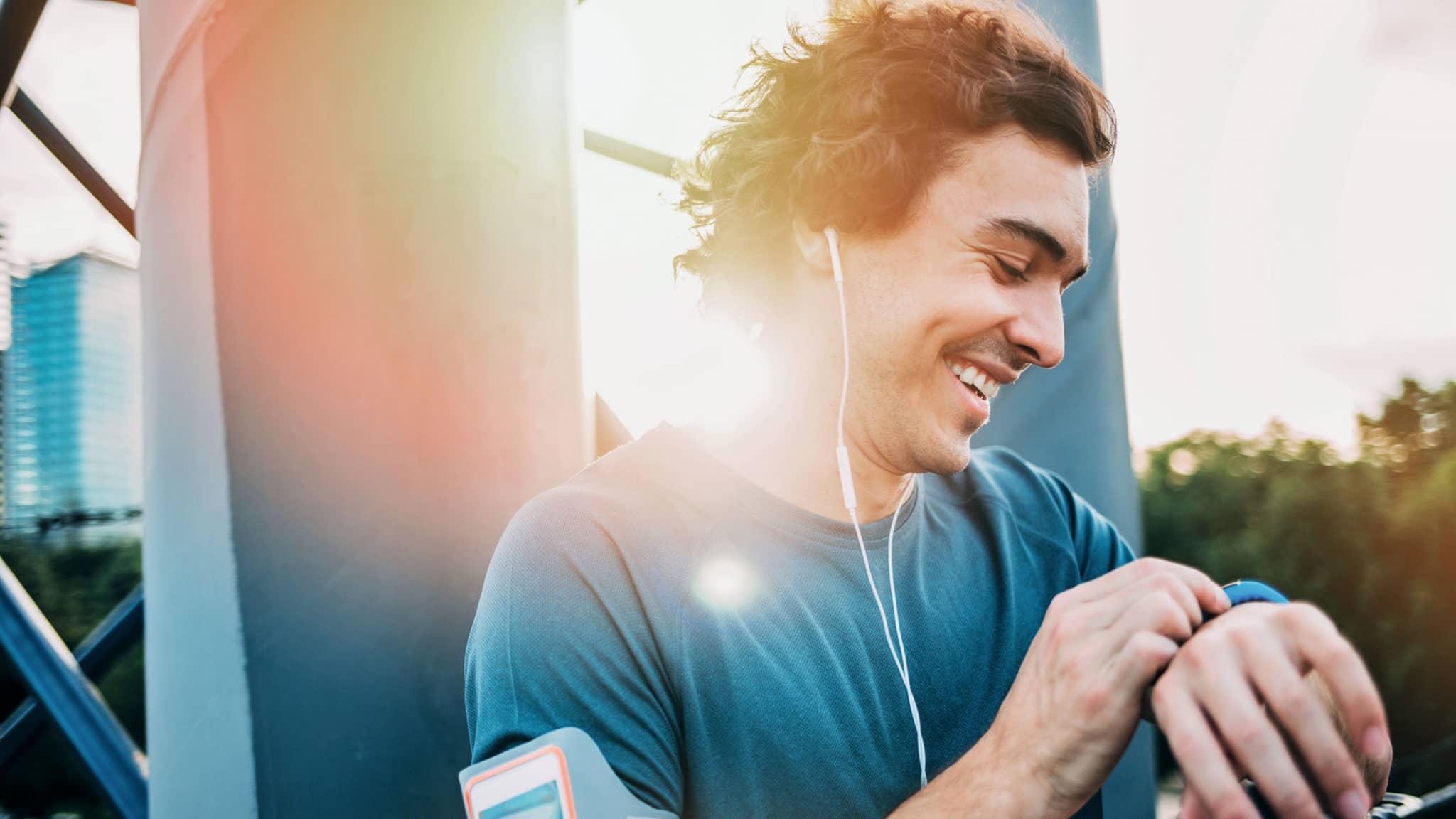 Junger sportlicher Mann guckt lachend auf seine Smartwatch nach seinem Lauf.
