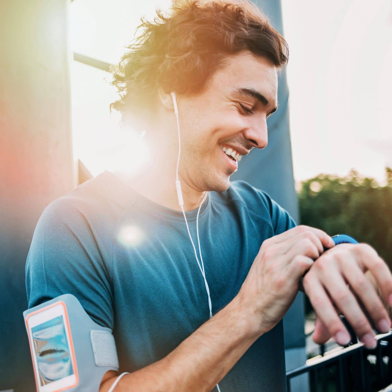 Junger sportlicher Mann guckt lachend auf seine Smartwatch nach seinem Lauf.