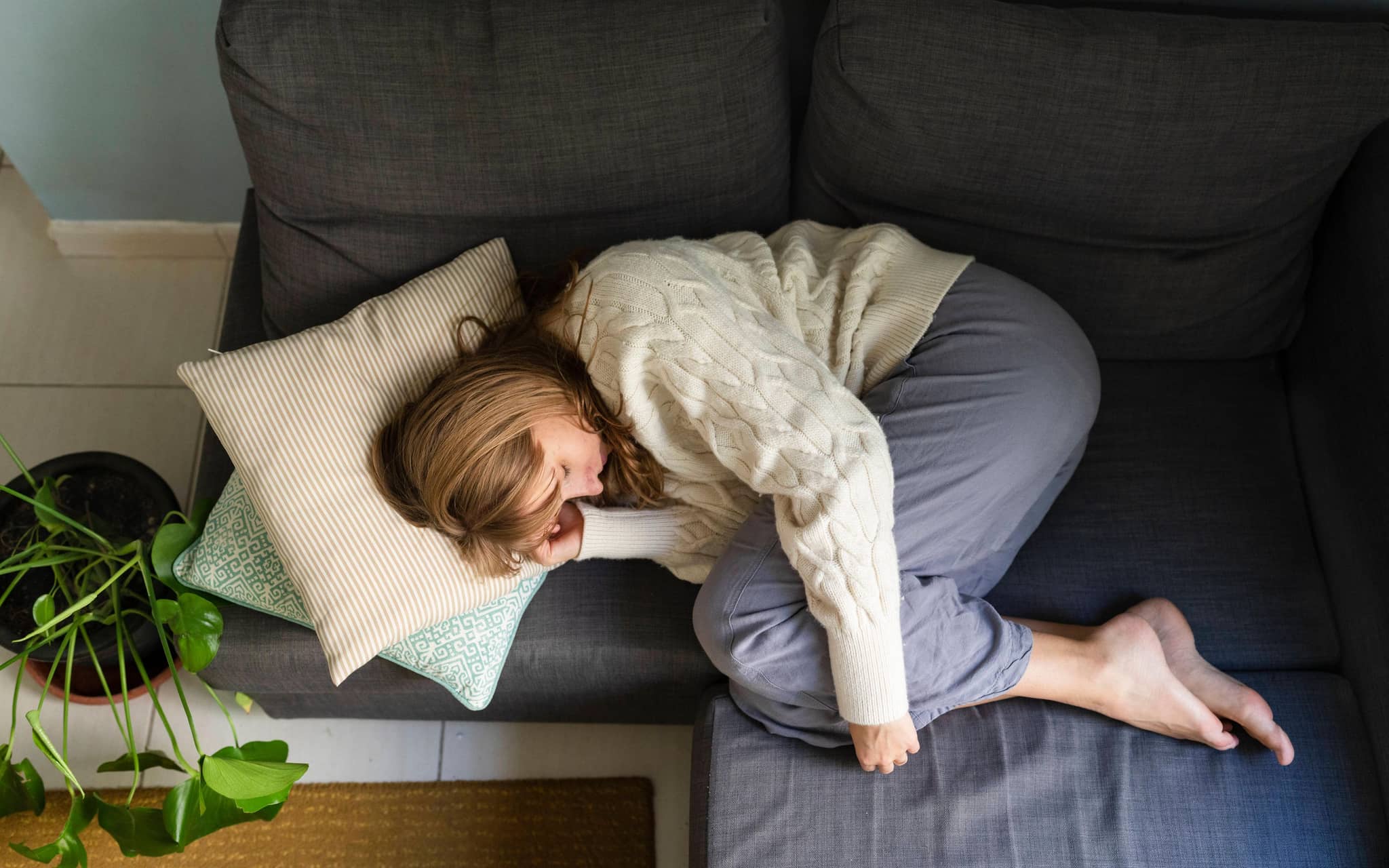 Junge Frau liegt gekrümmt auf der Couch.