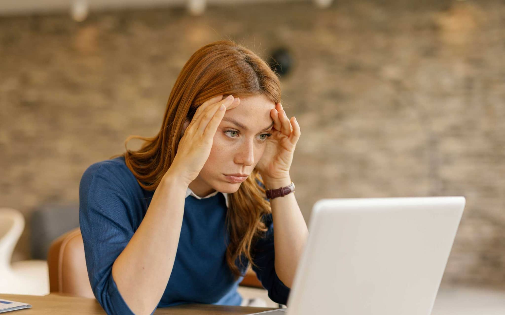 Junge Frau fasst sich erschöpft ins Gesicht und schaut auf einen Laptop