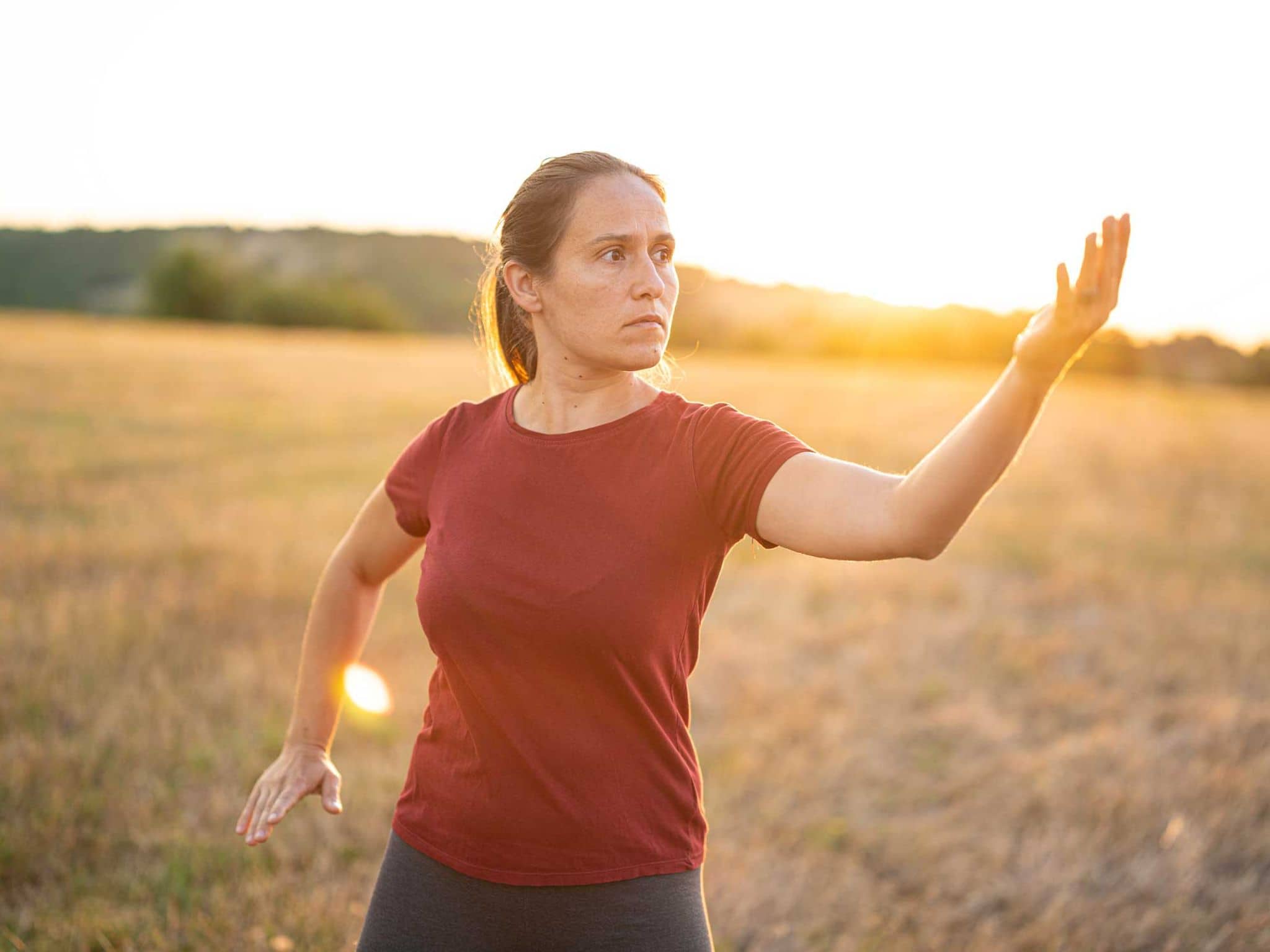 Eine Frau steht auf einer Wiese und macht Qigong-Übungen