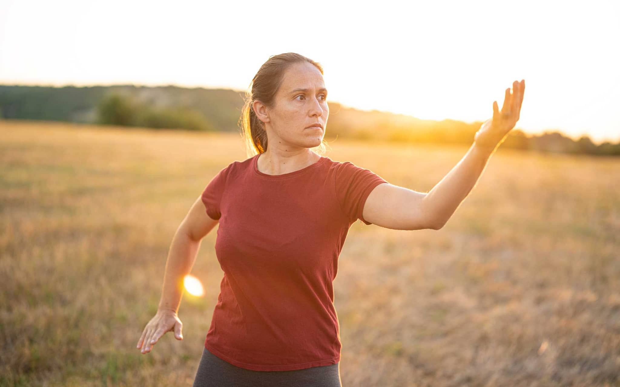 Eine Frau steht auf einer Wiese und macht Qigong-Übungen