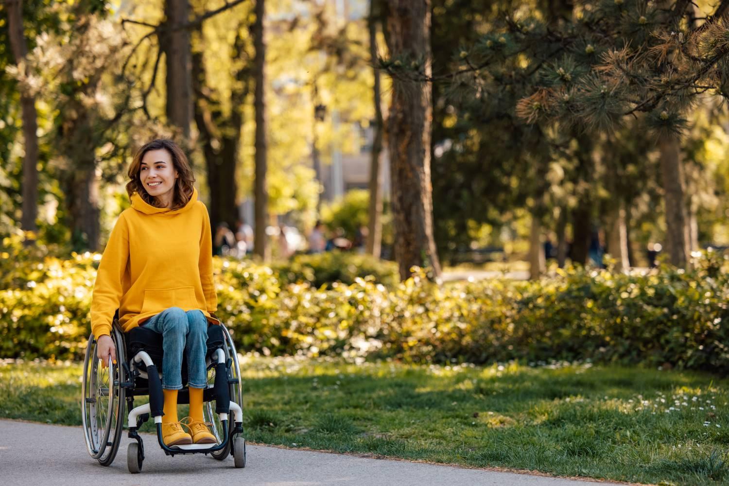 Rollstühle: Junge Frau fährt im Rollstuhl durch den sonnigen Park.
