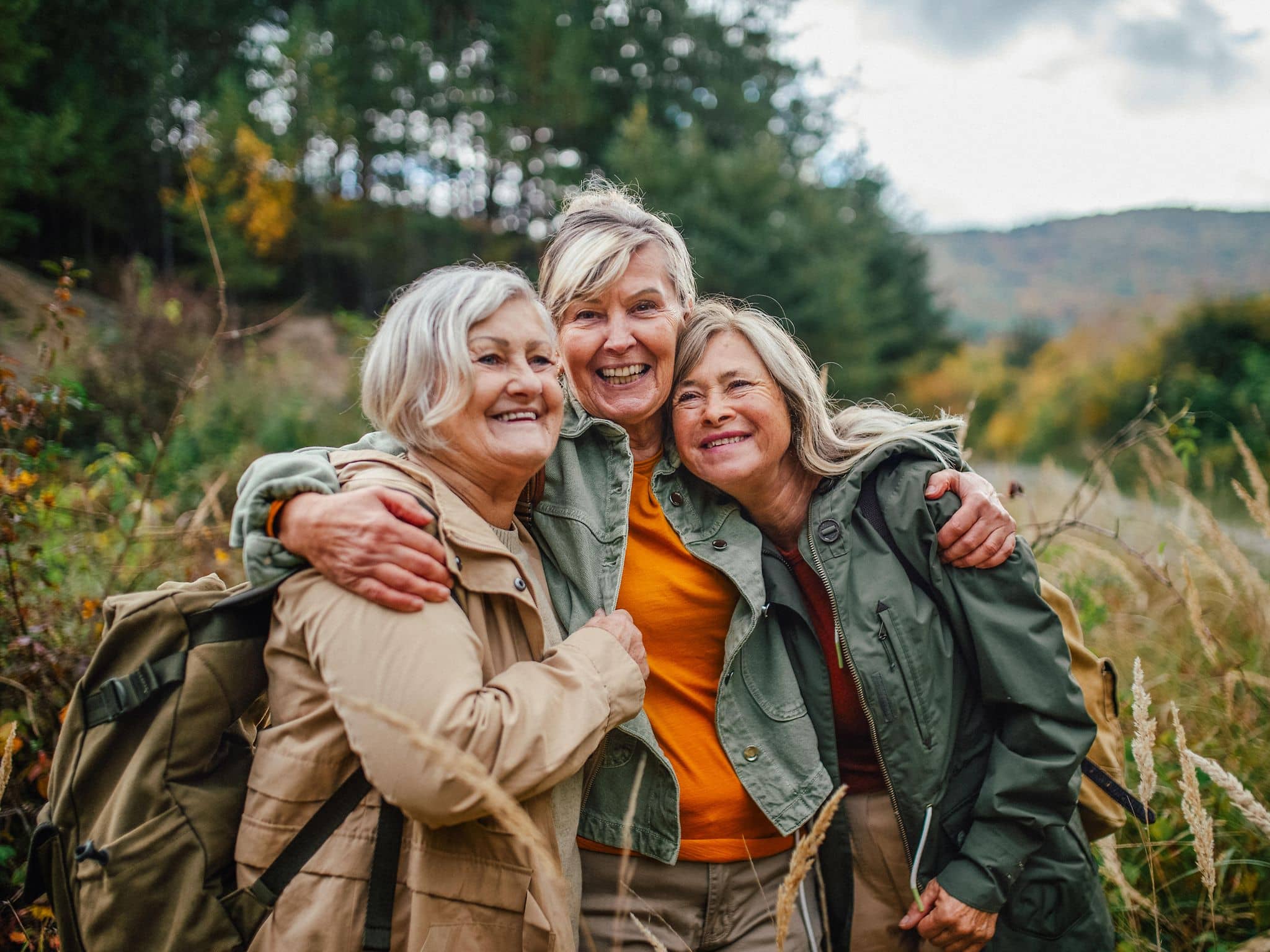 Drei ältere Frauen in der Natur umarmen sich.