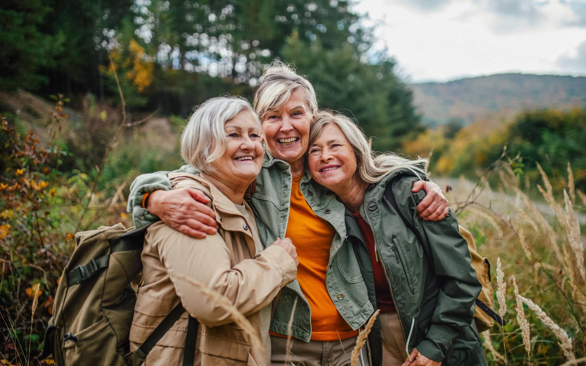 Drei ältere Frauen in der Natur umarmen sich.