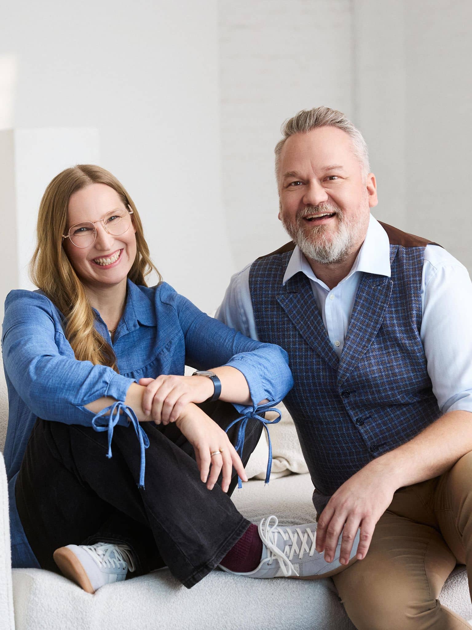 Fröhliche Frau Franca Cerutti und Mann Christian Weiss,sitzen auf einem weißen Sofa.