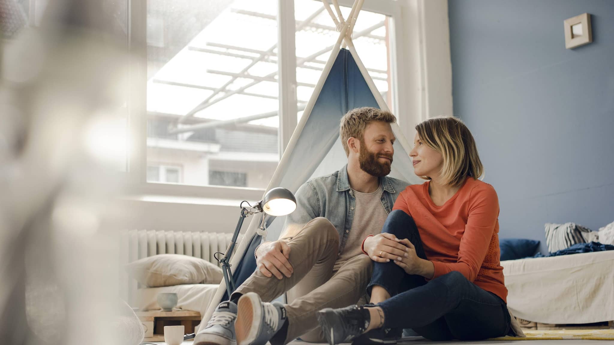 Mann und Frau sitzen auf dem Boden vor einem Kinderzelt und schauen sich an.