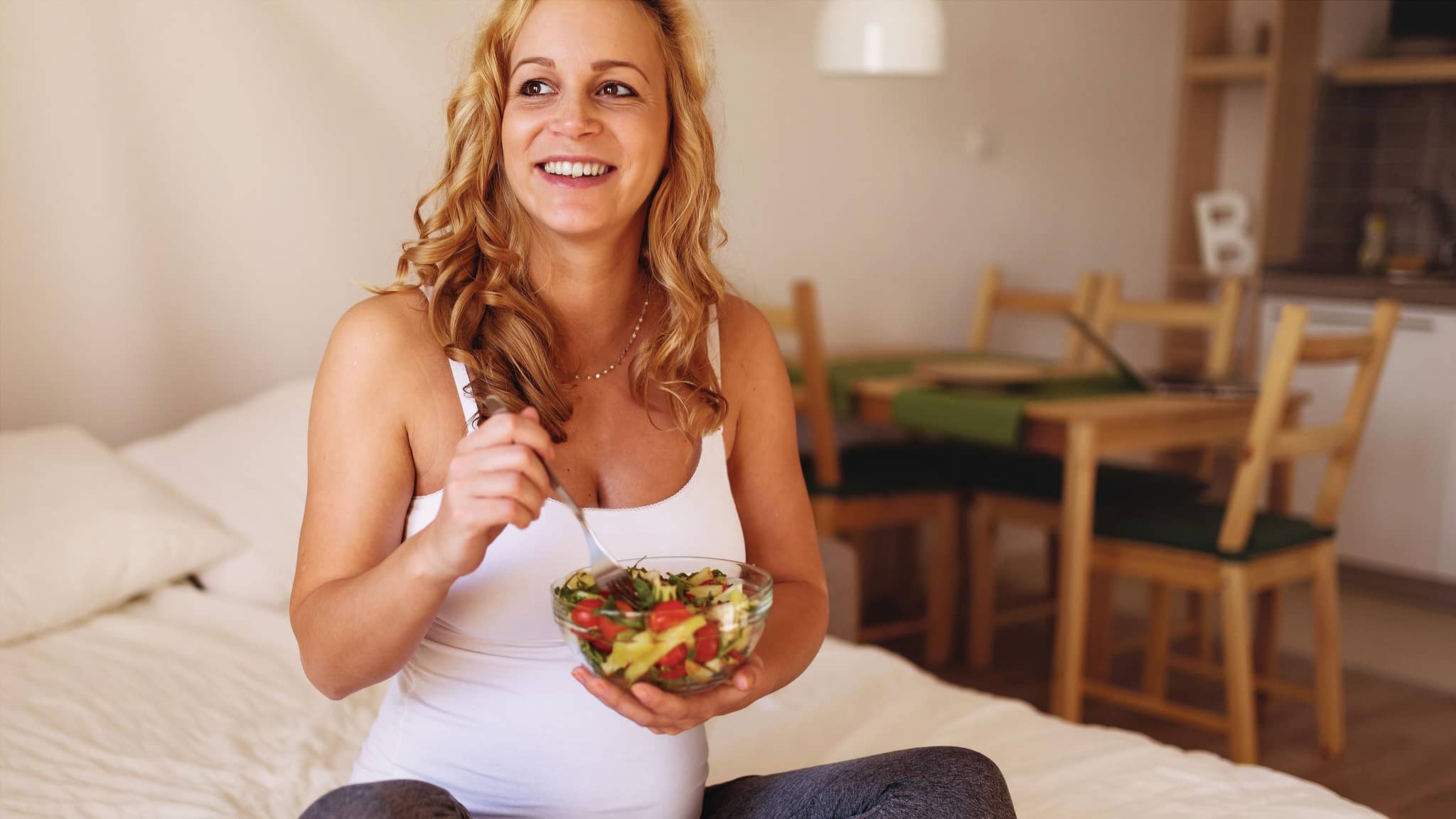 Schwangere Frau isst Salat auf dem Bett