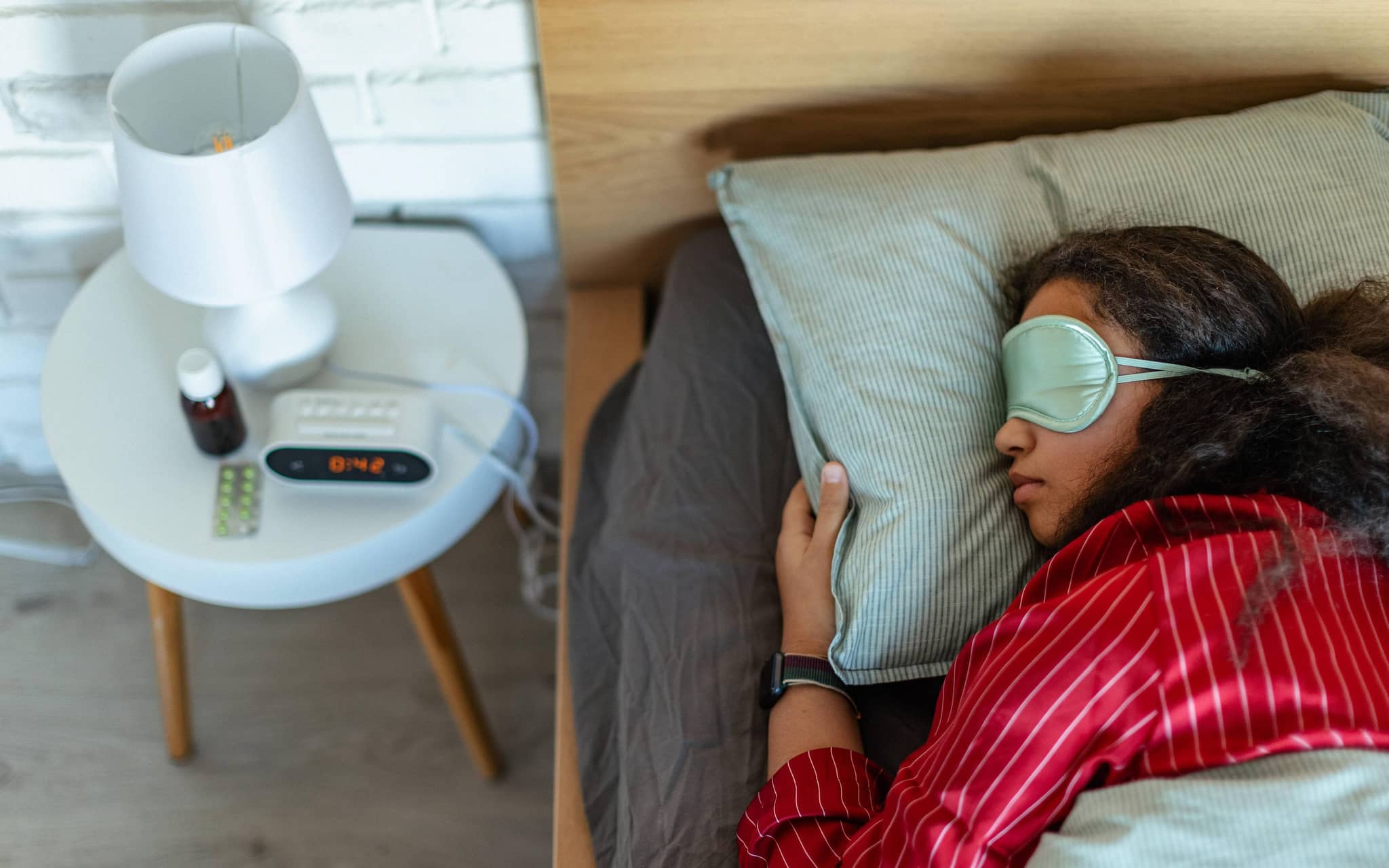 Eine Frau liegt schlafend im Bett, auf dem Nachttisch sieht man Melatonin-Präparate, die beim Einschlafen helfen sollen.