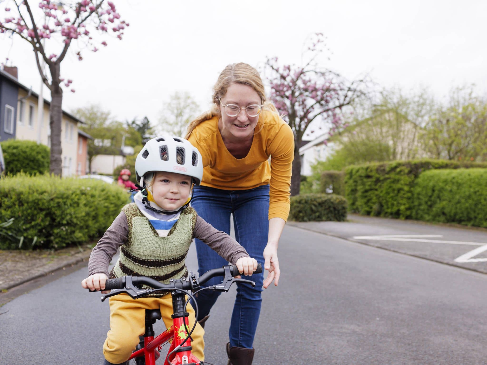 Eine Mutter hilft ihrem Kind, das einen Helm trägt, Fahrradfahren zu lernen.