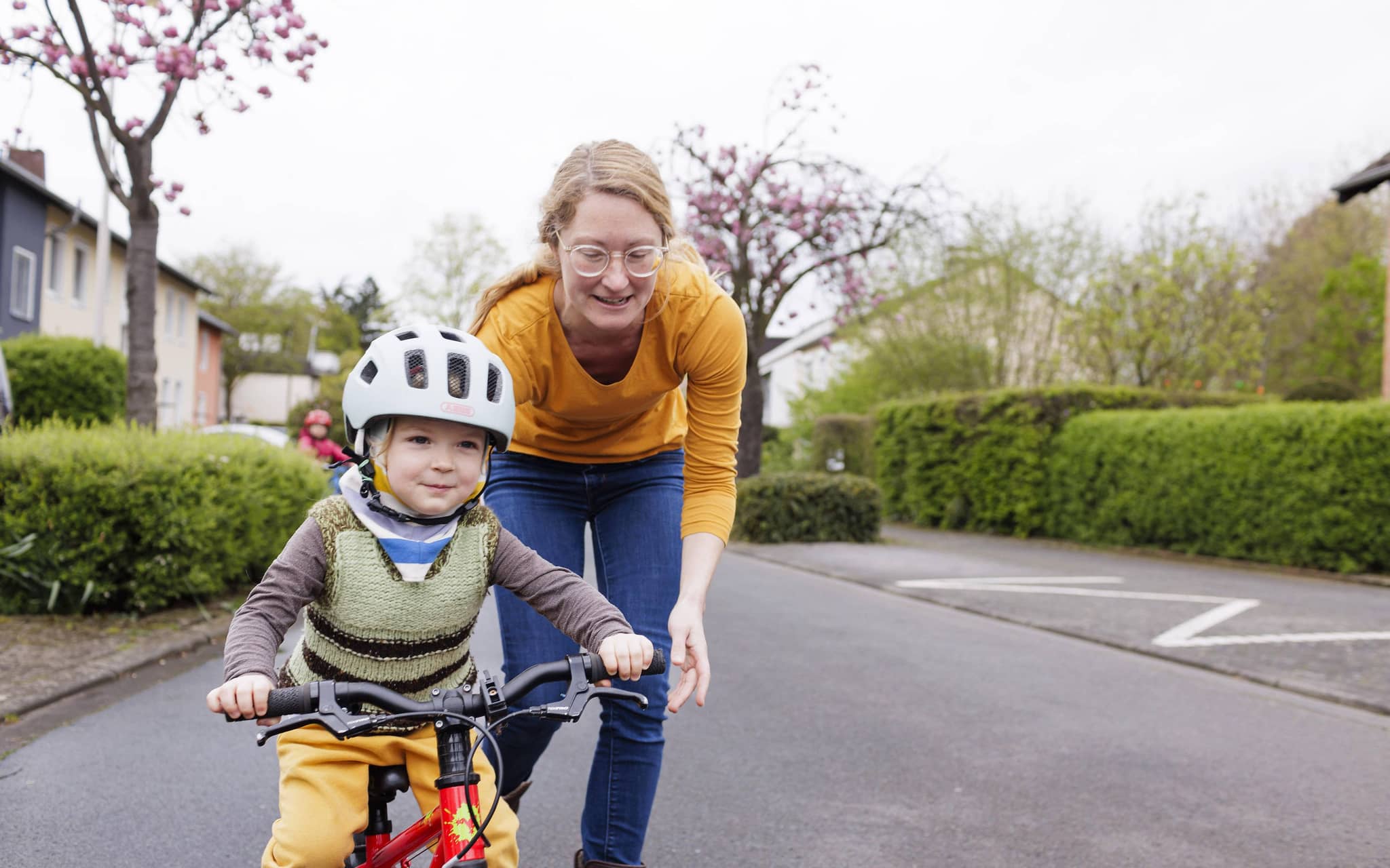Eine Mutter hilft ihrem Kind, das einen Helm trägt, Fahrradfahren zu lernen.