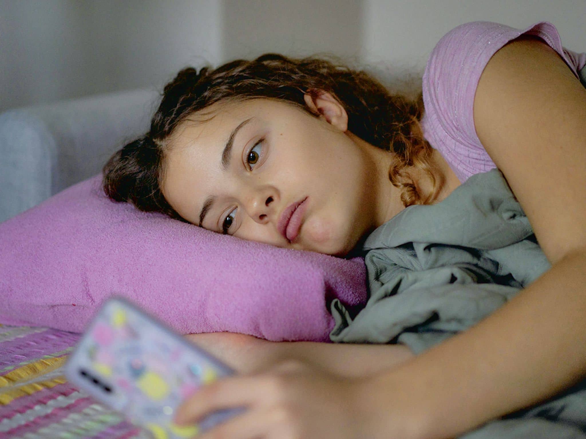 Online-Shopping: Junges Mädchen liegt in ihrem Bett und schaut verträumt auf ihr Handy.