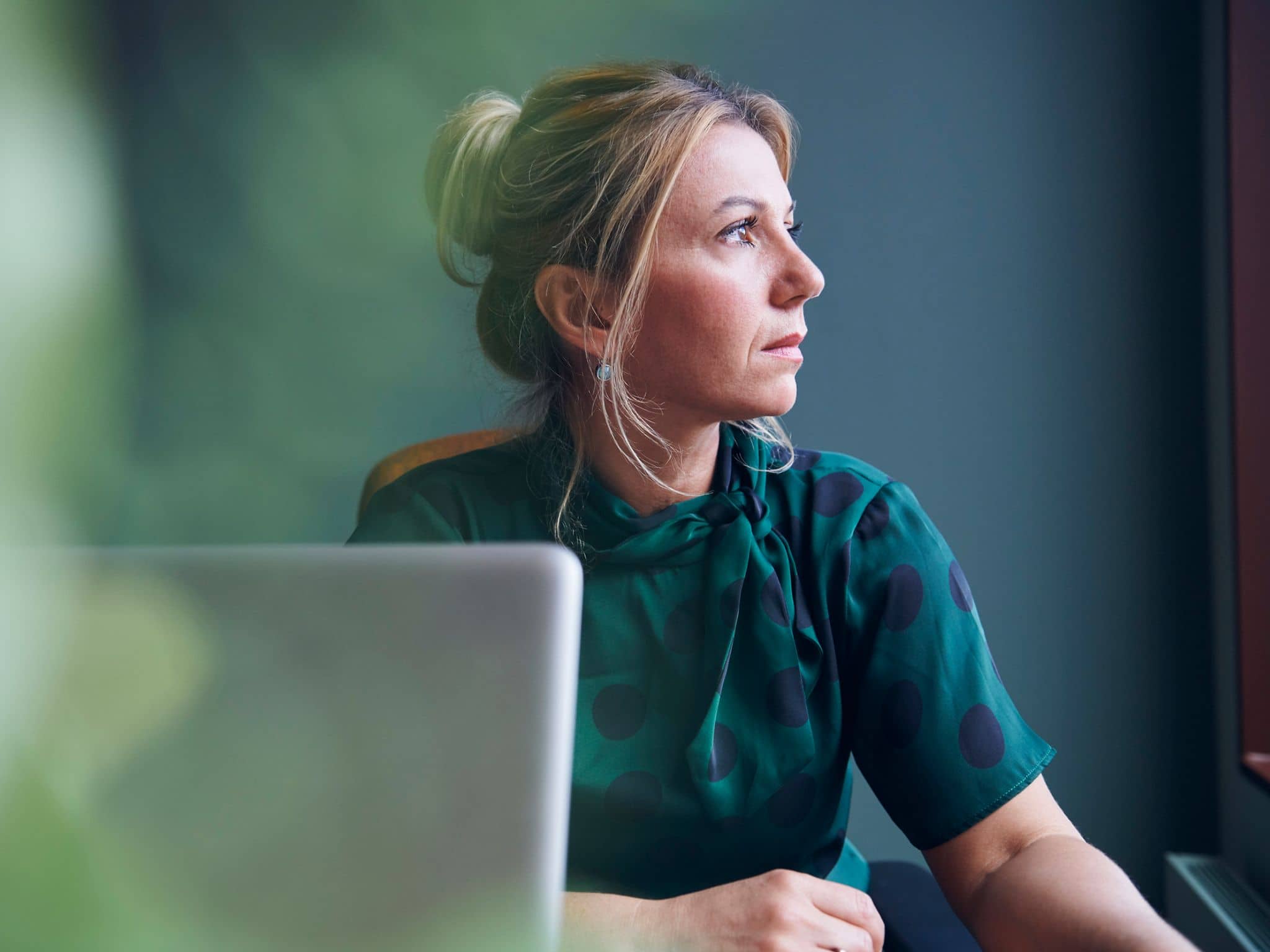 Hochfunktionale Depression: Gepflegte Frau vor einem PC schaut traurig zur Seite.